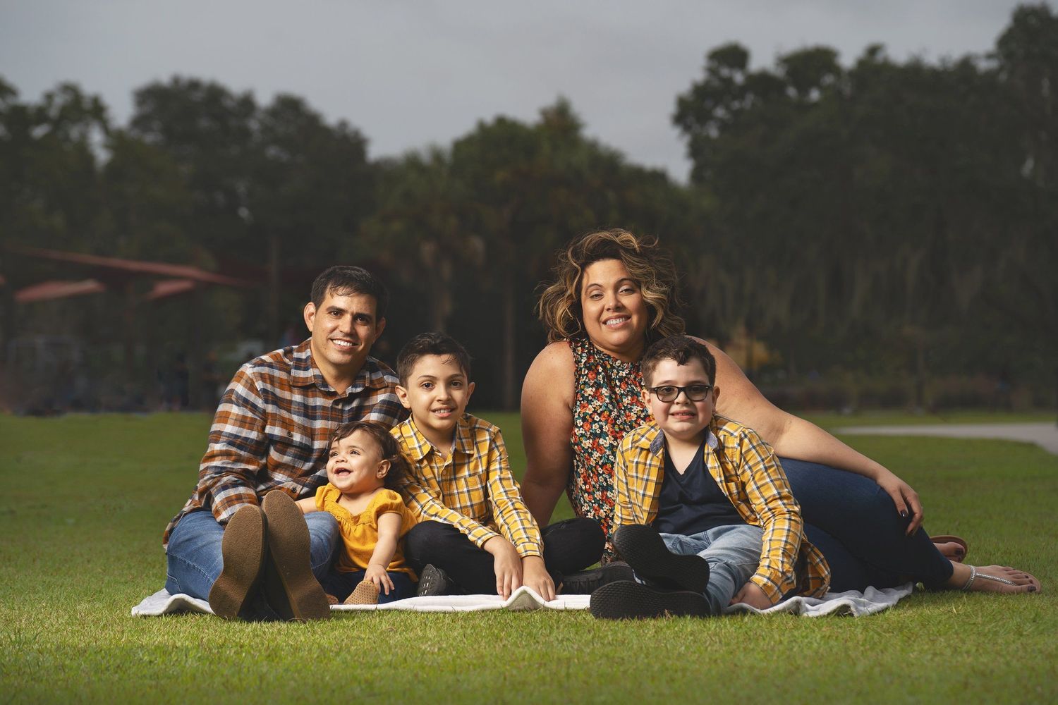 A family relaxes together on a blanket in a grassy field during golden hour.