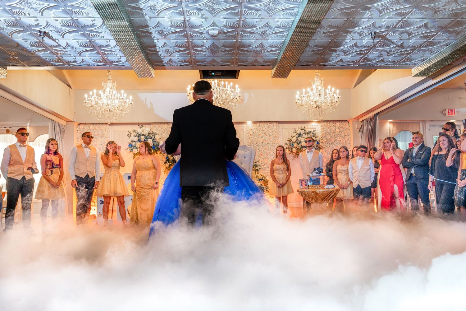Wedding reception guests dance together under elegant chandeliers with fog effects on the dance floor.