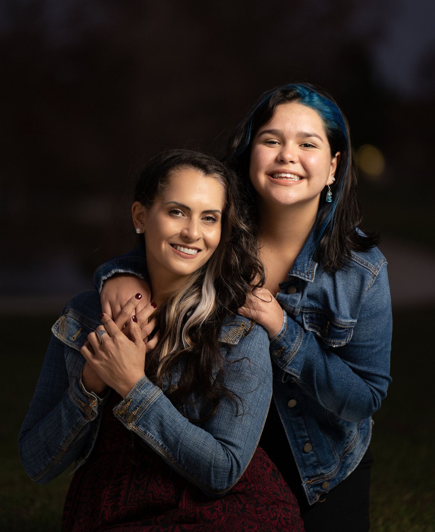 Two people in denim jackets share a joyful embrace while posing outdoors.