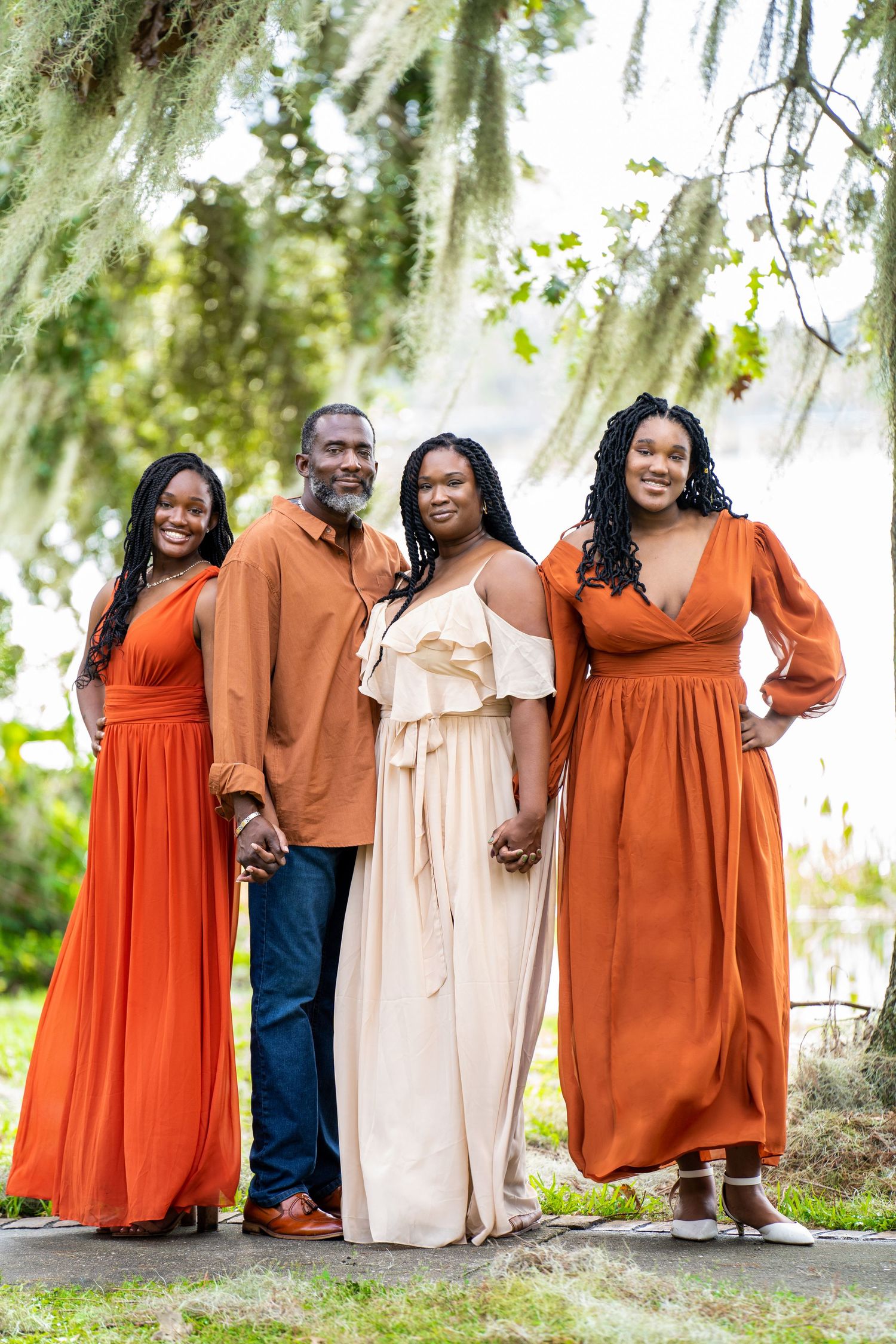 Family of four posing outdoors in coordinating orange and cream outfits under moss-draped trees.