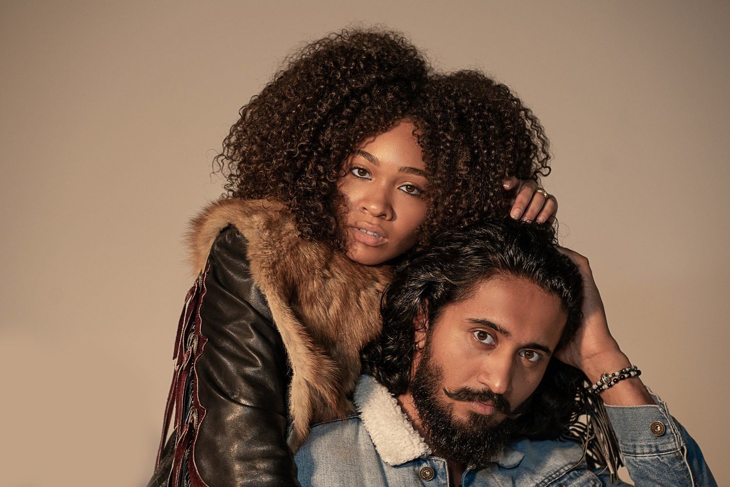 A stylish couple in leather jackets poses against a neutral background.