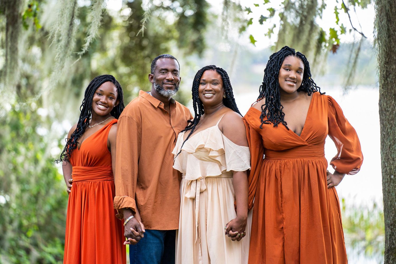 A group poses outdoors wearing coordinated orange dresses and brown attire.