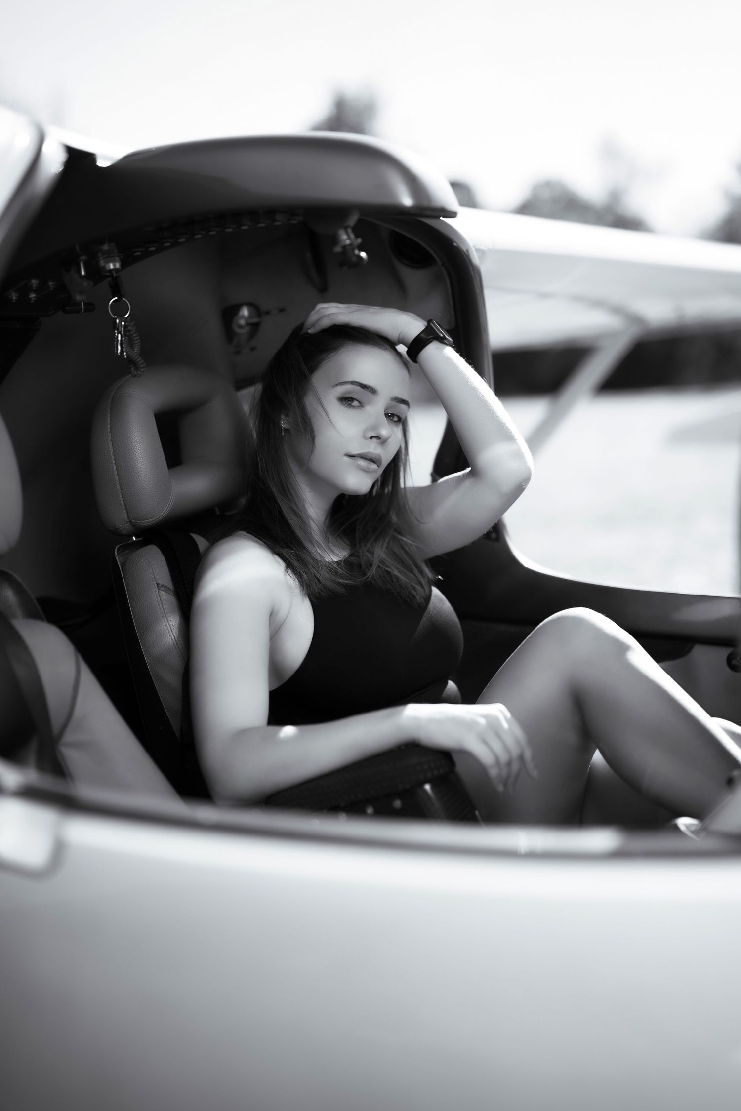 Black and white photo of a young woman in a black dress posing elegantly inside a small aircraft cockpit.
