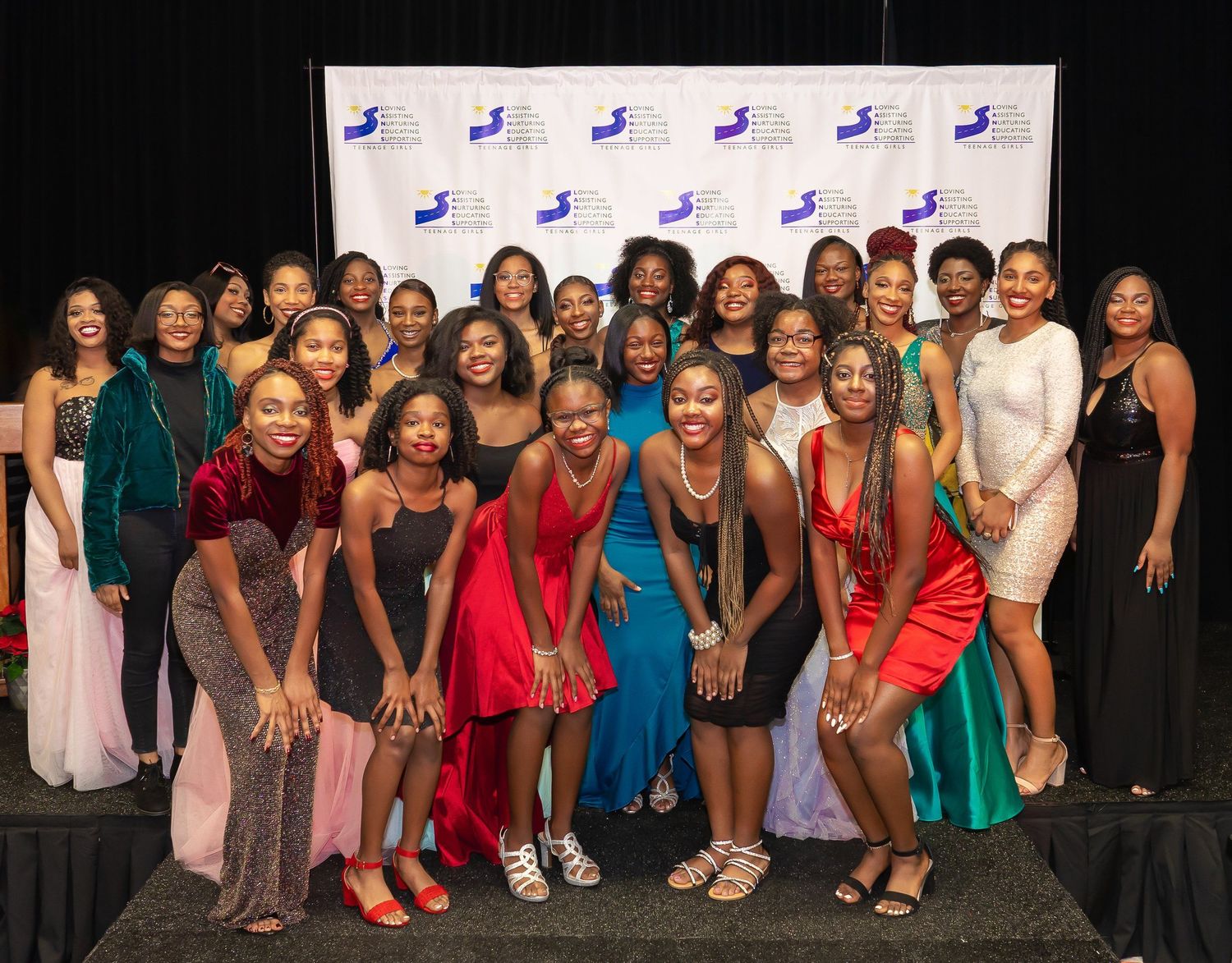 Large group of Black women in elegant formal attire posing together at a gala event.