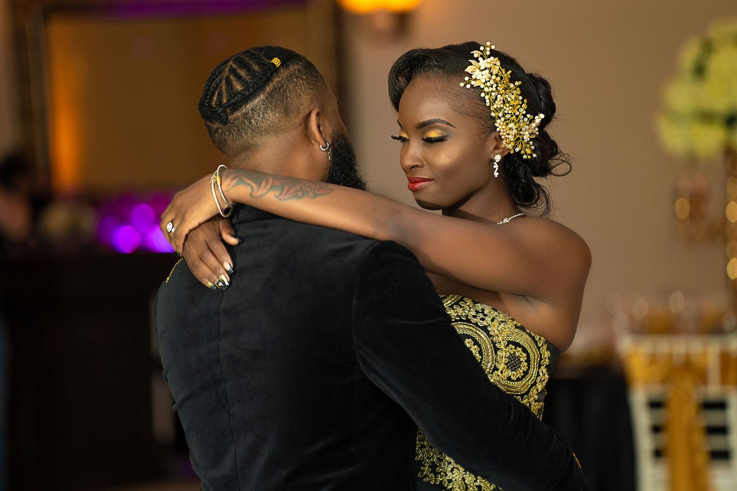 Couple sharing a romantic first dance at a wedding reception, bride in gold and black gown with floral hair accessory.
