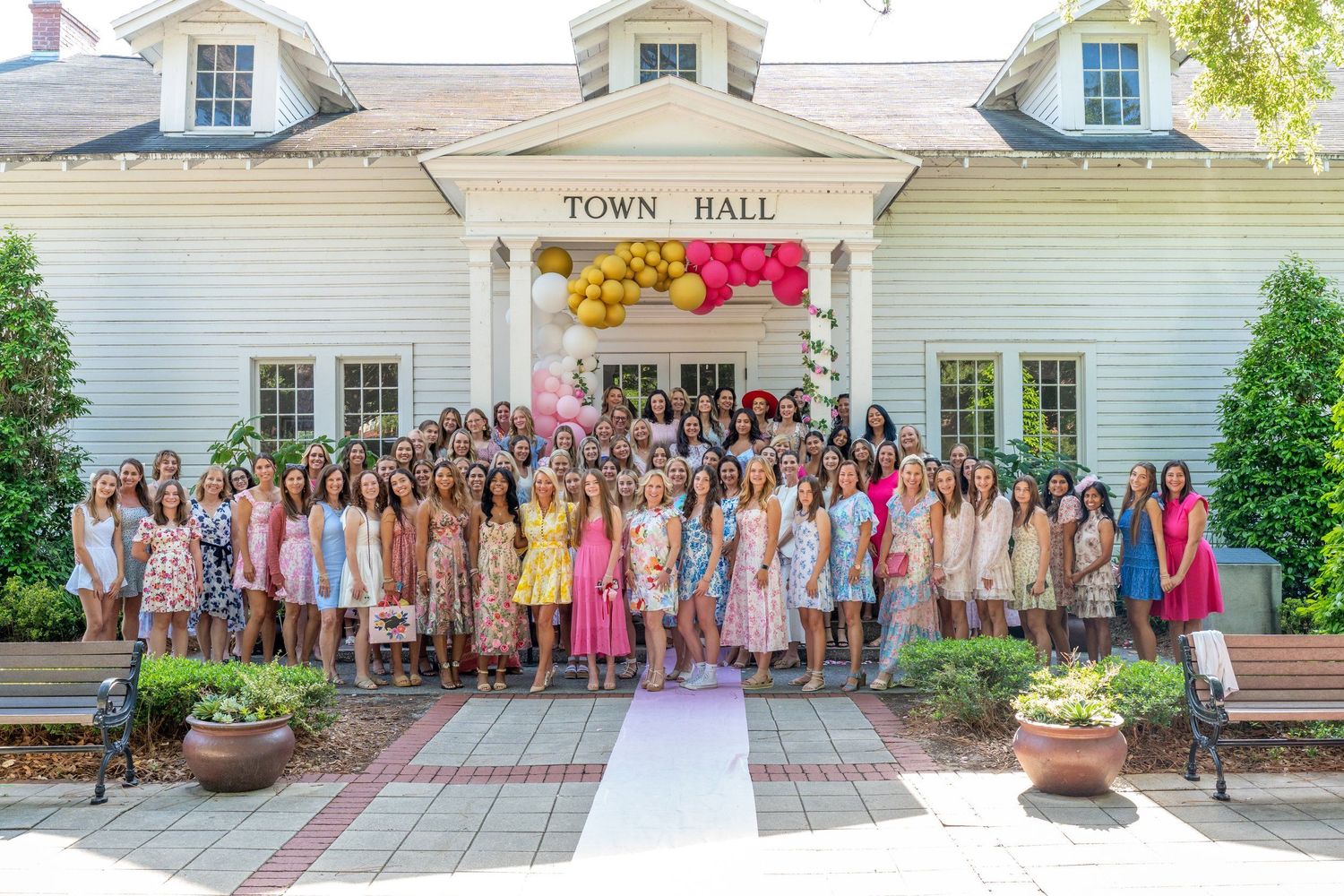 Large group poses outside a white town hall building for formal event photos.