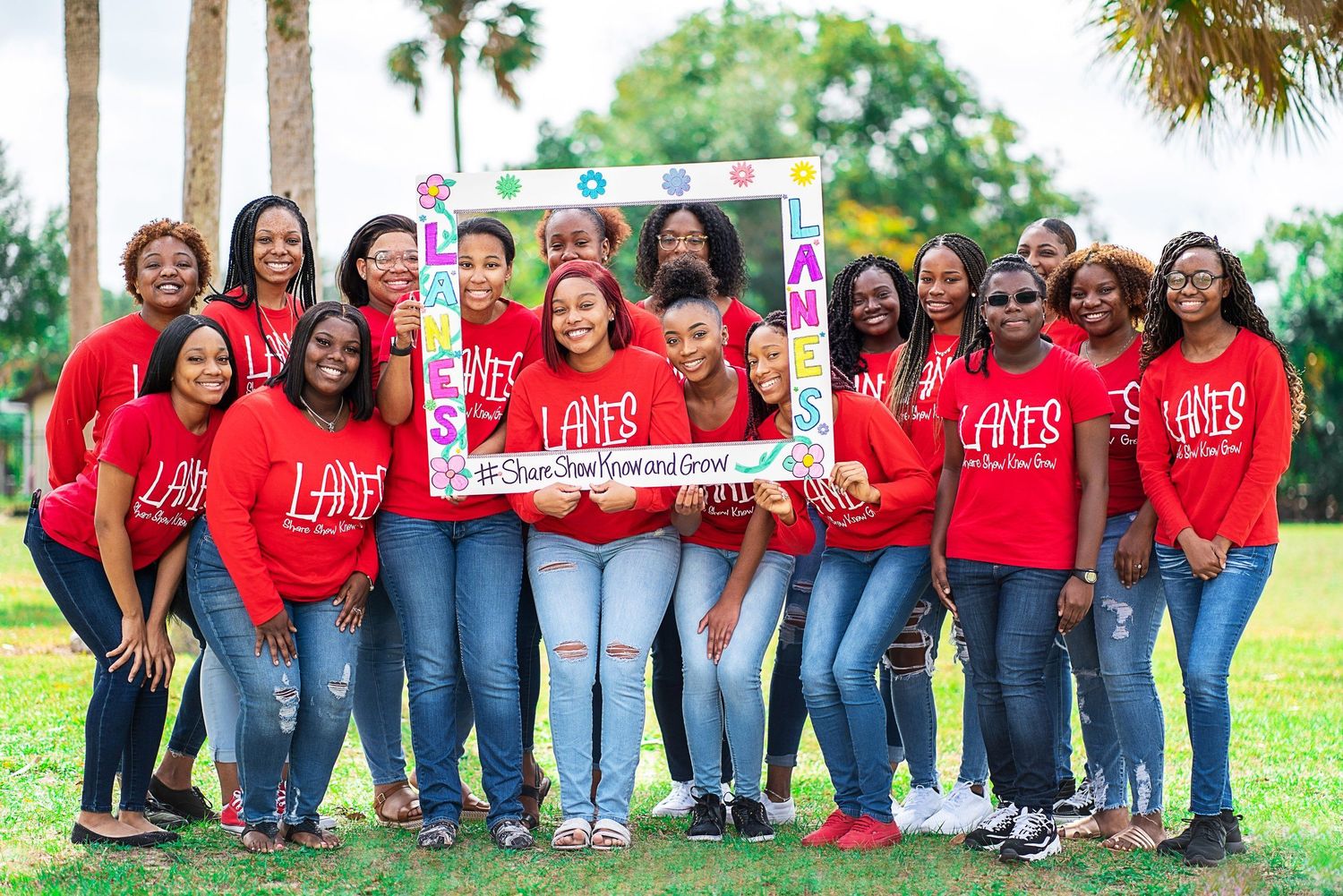 Group of women in matching red LANES t-shirts posing outdoors with a decorative photo frame at a community event.