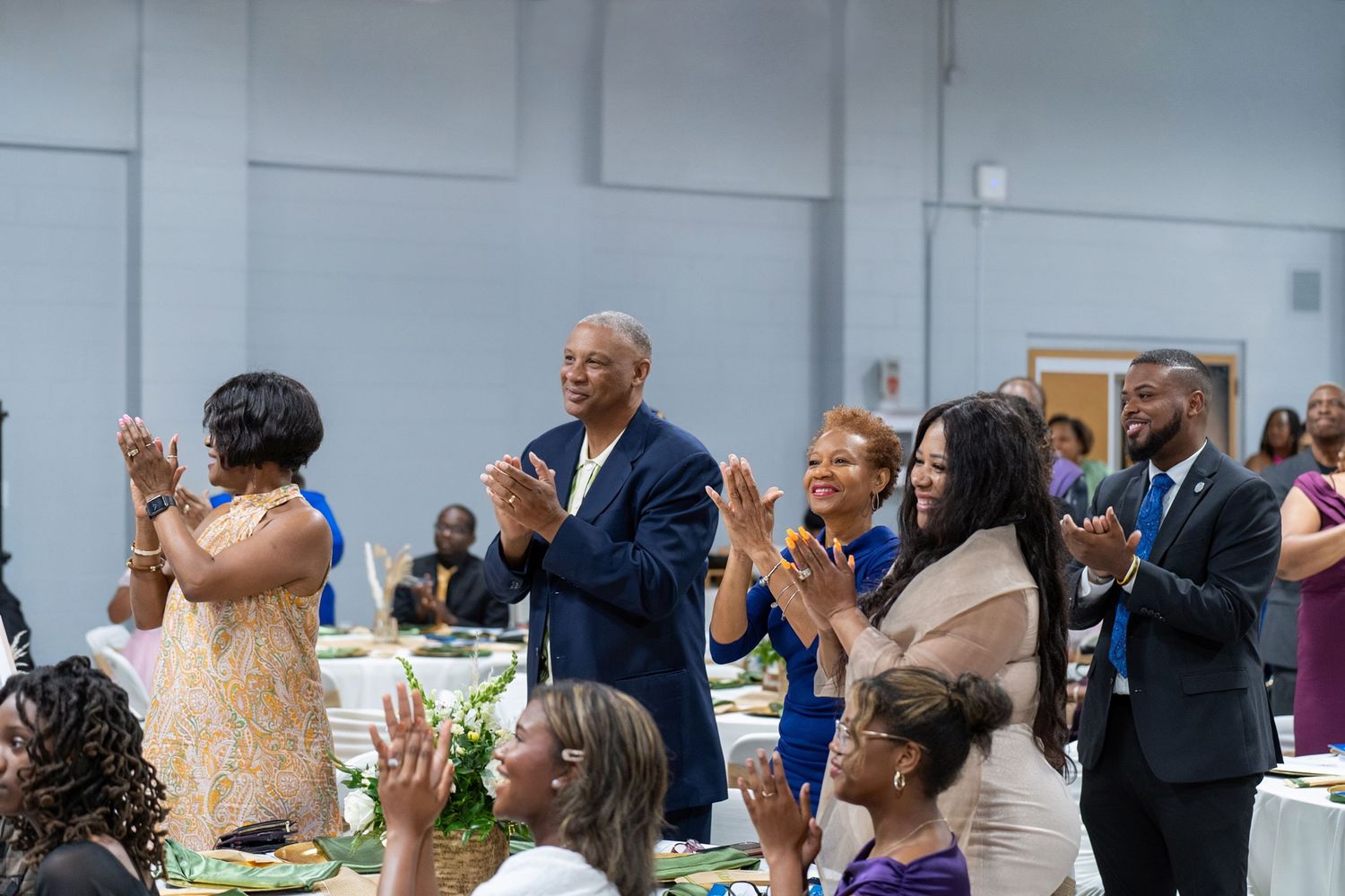 Guests applaud and celebrate at a formal banquet event in a large hall with decorated tables.