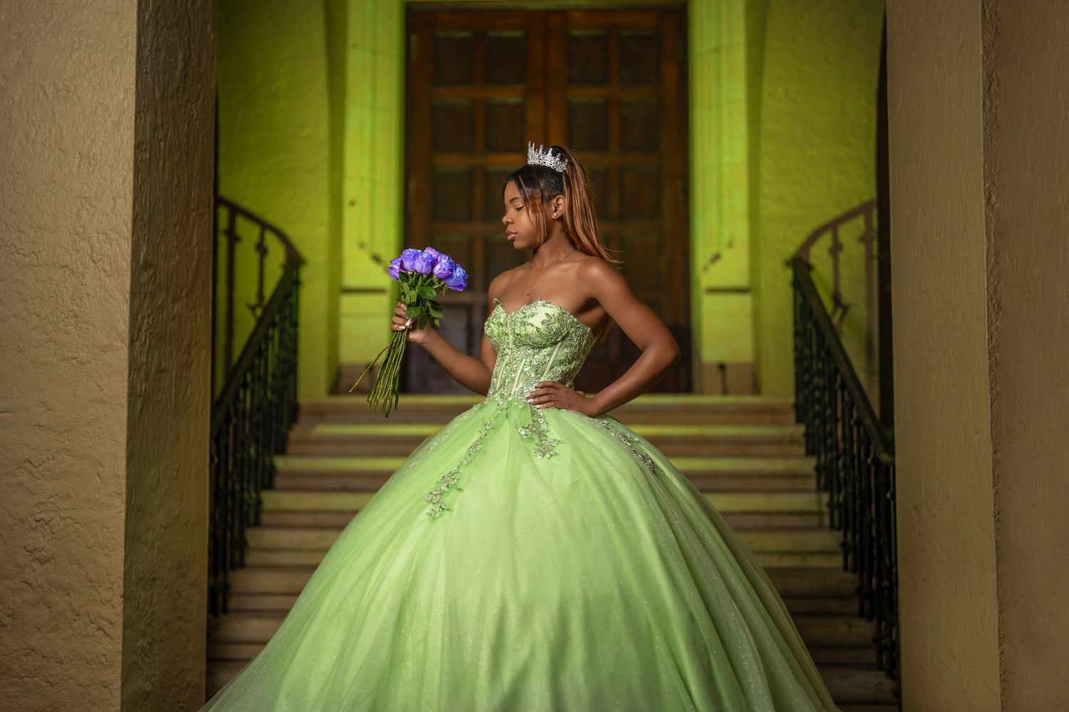 A stunning lime green quinceañera ball gown photographed against an elegant entrance with wrought iron railings.