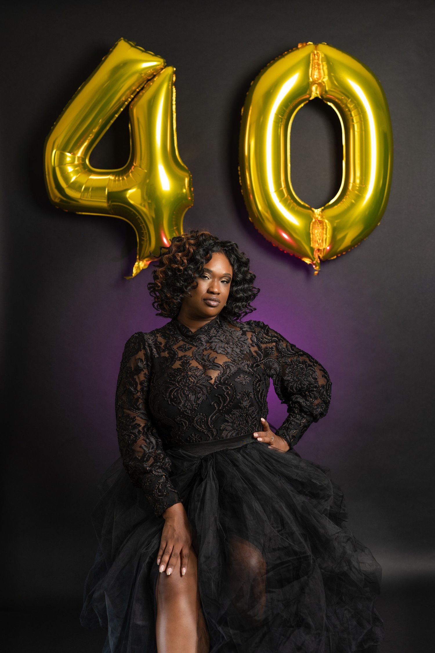 Woman in black lace gown posing elegantly in front of gold number 40 balloons for a milestone birthday celebration.