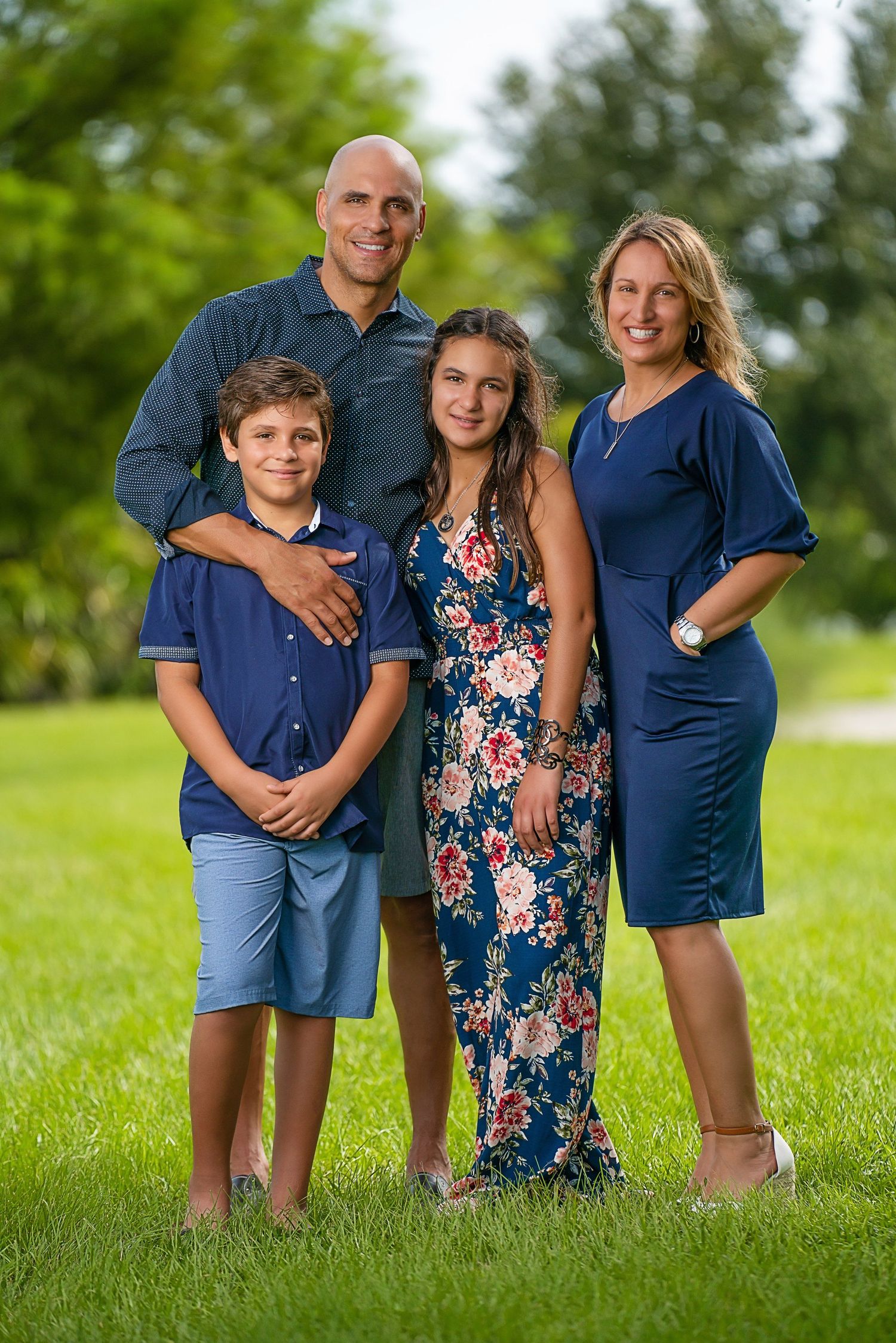 A family of four poses together on grass wearing coordinated blue outfits.