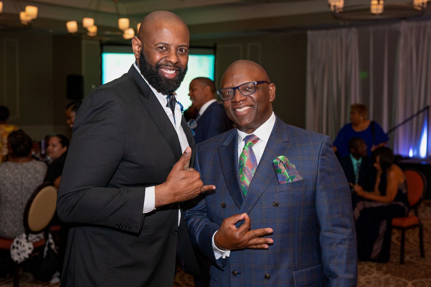 Two well-dressed men in suits smiling and posing together at a formal event or gala celebration.