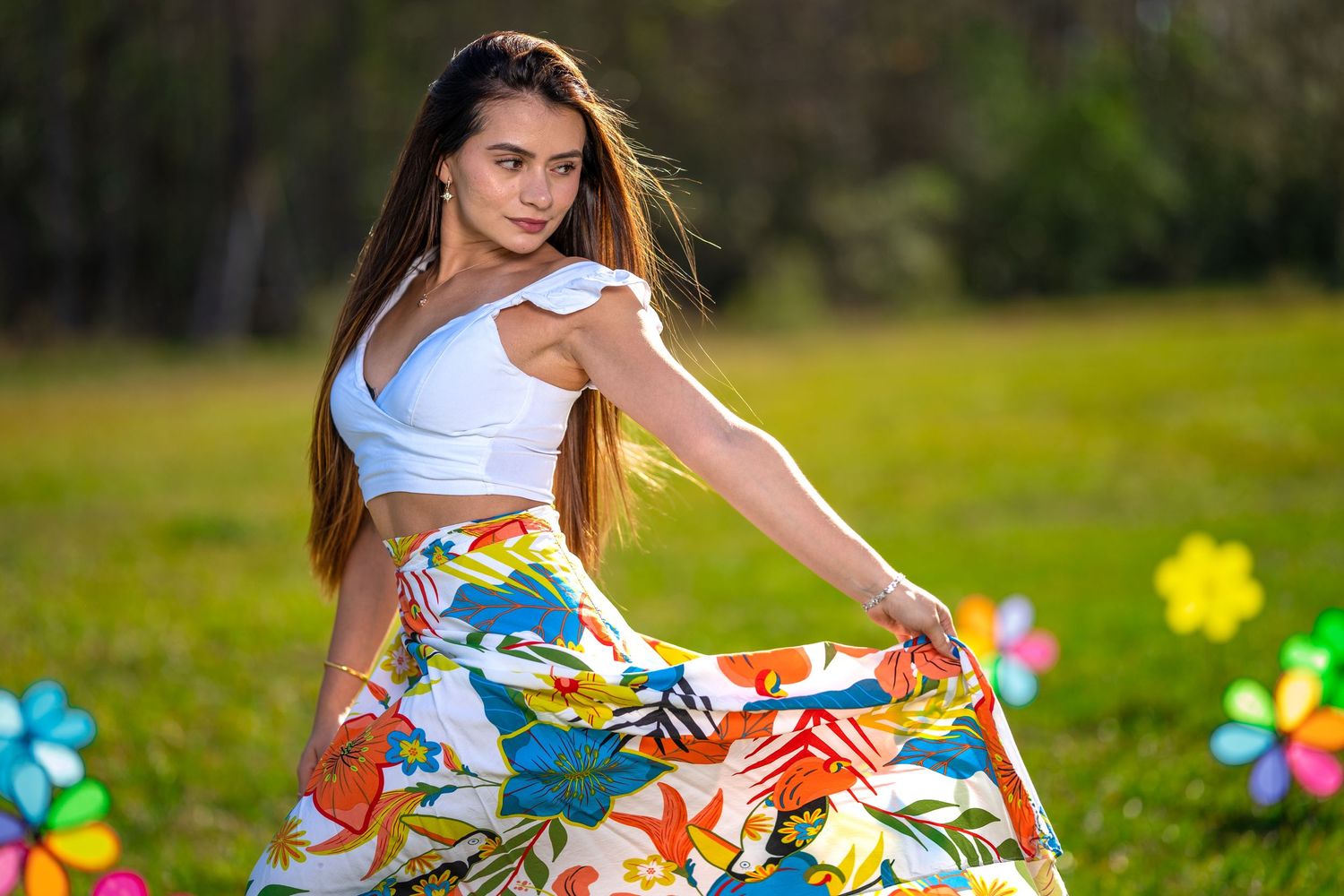Woman in colorful floral dress twirls playfully in a sunny outdoor garden setting.