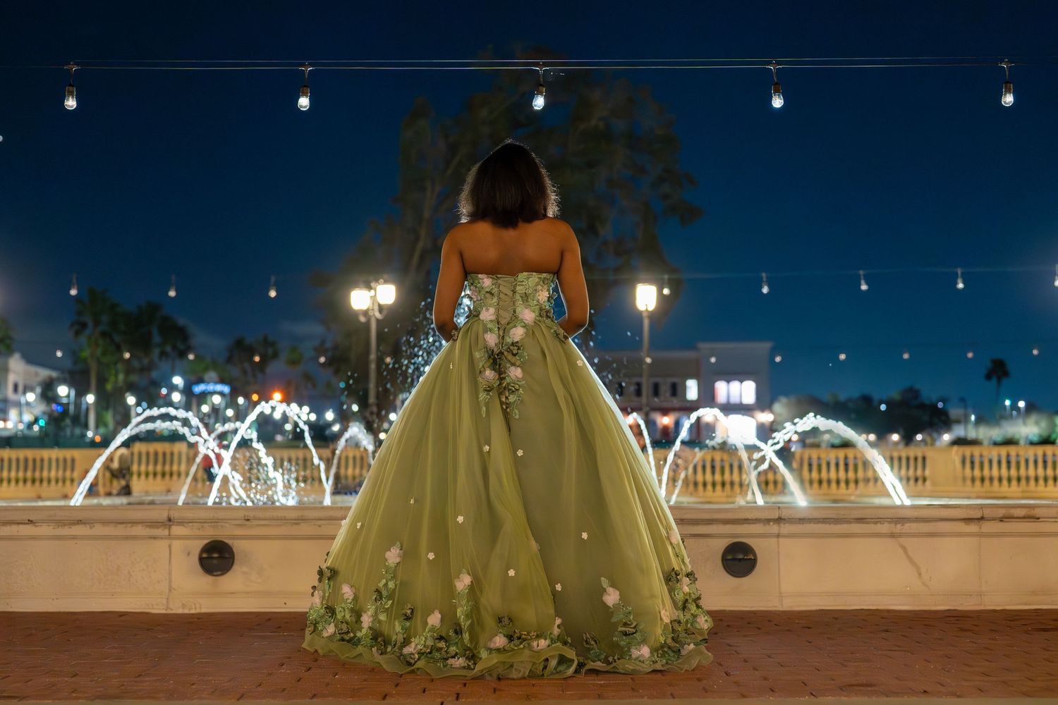 Mint green ball gown photographed at night with twinkling lights in background.
