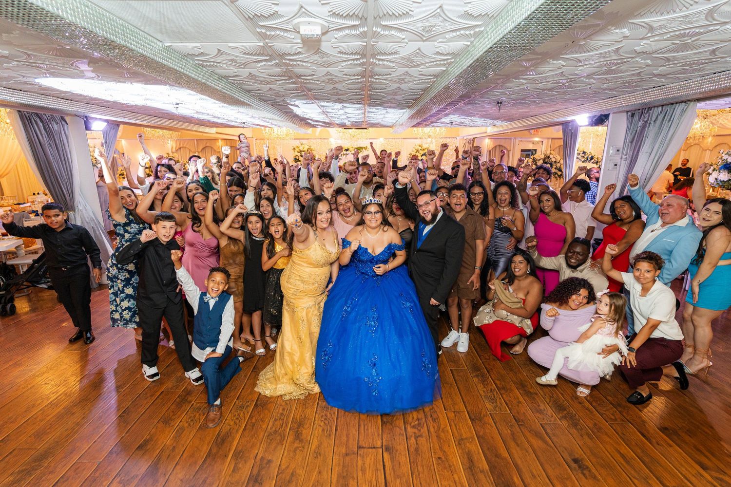 Large diverse group celebrating at a quinceañera with a girl in a blue ball gown.
