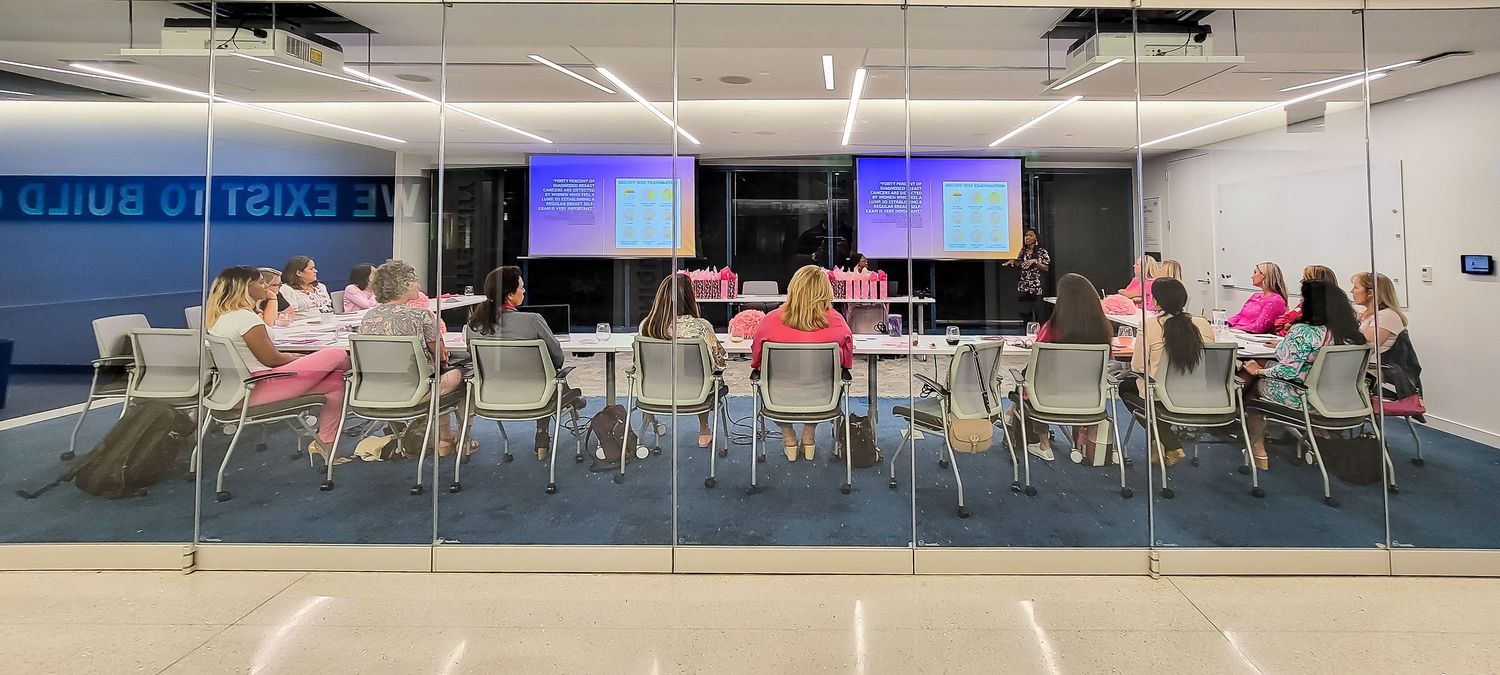 Group of professionals attending a presentation in a modern glass-walled conference room with blue carpet.