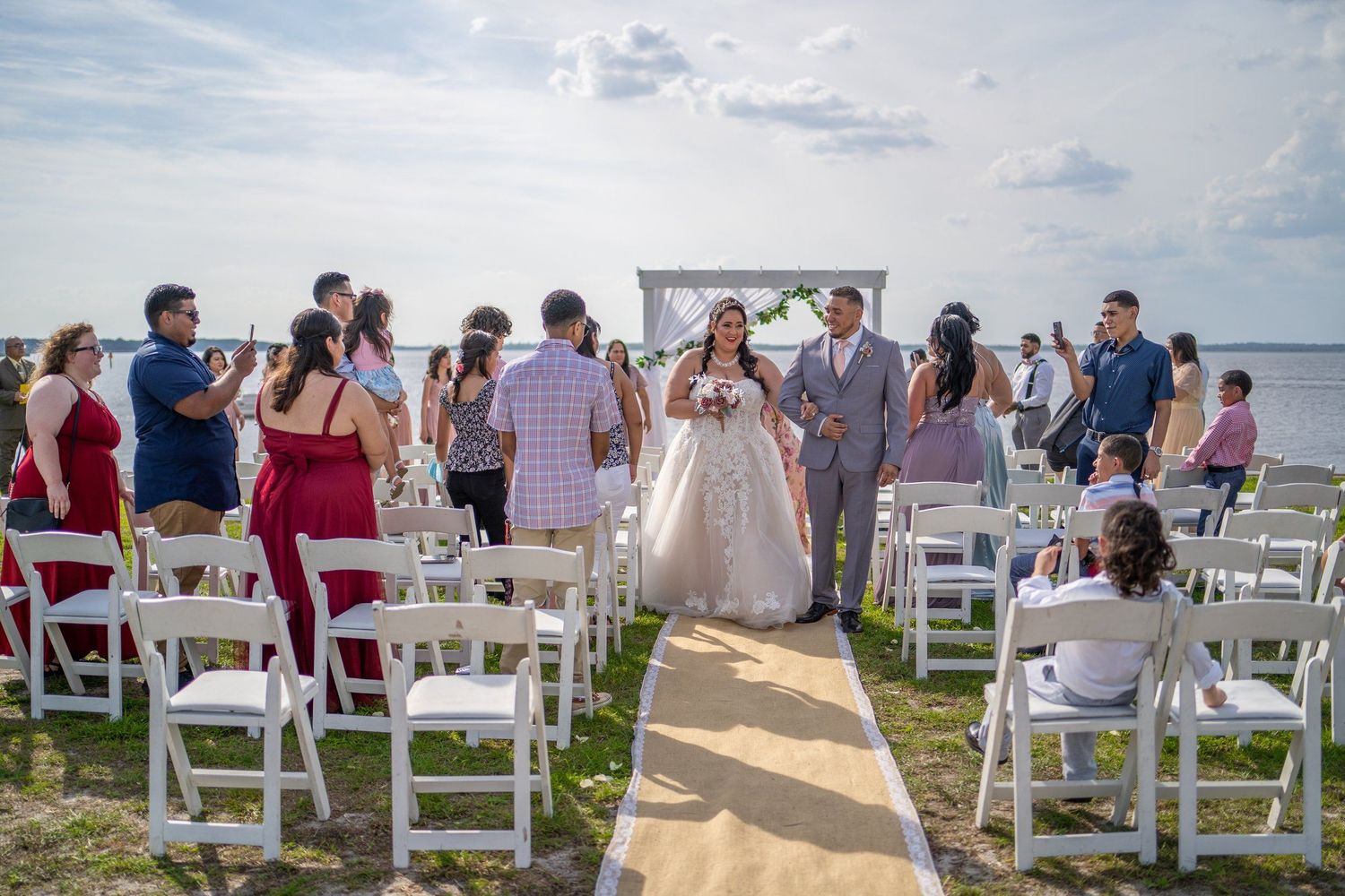 White chairs line an outdoor ceremony aisle with ocean views and blue skies.