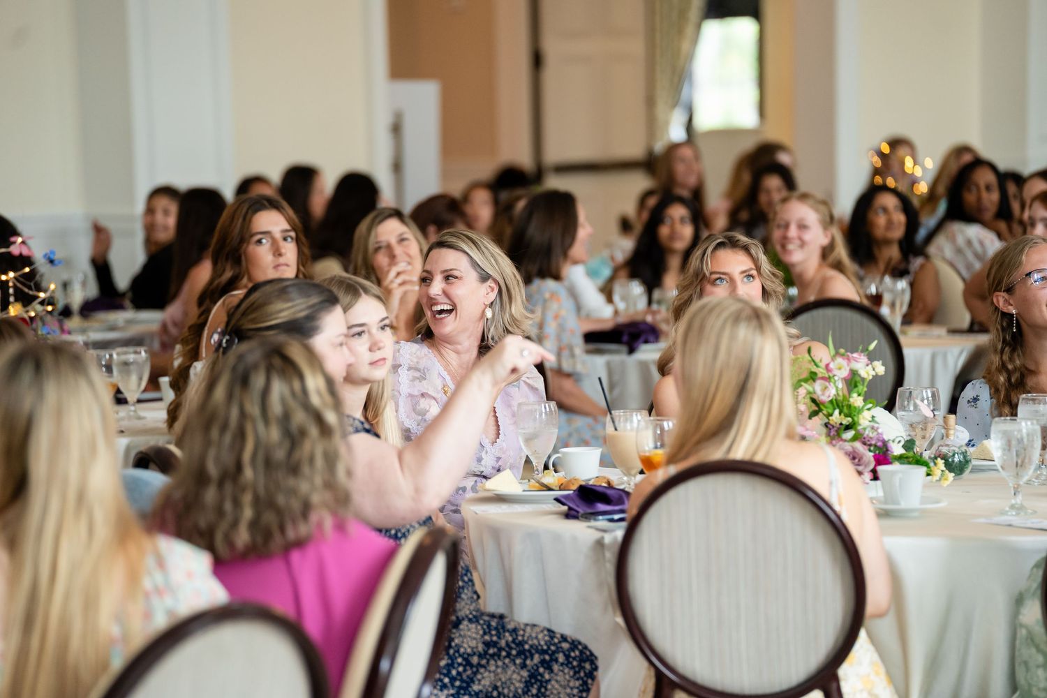 Women laughing and socializing at elegant banquet tables during a formal daytime event or luncheon gathering.