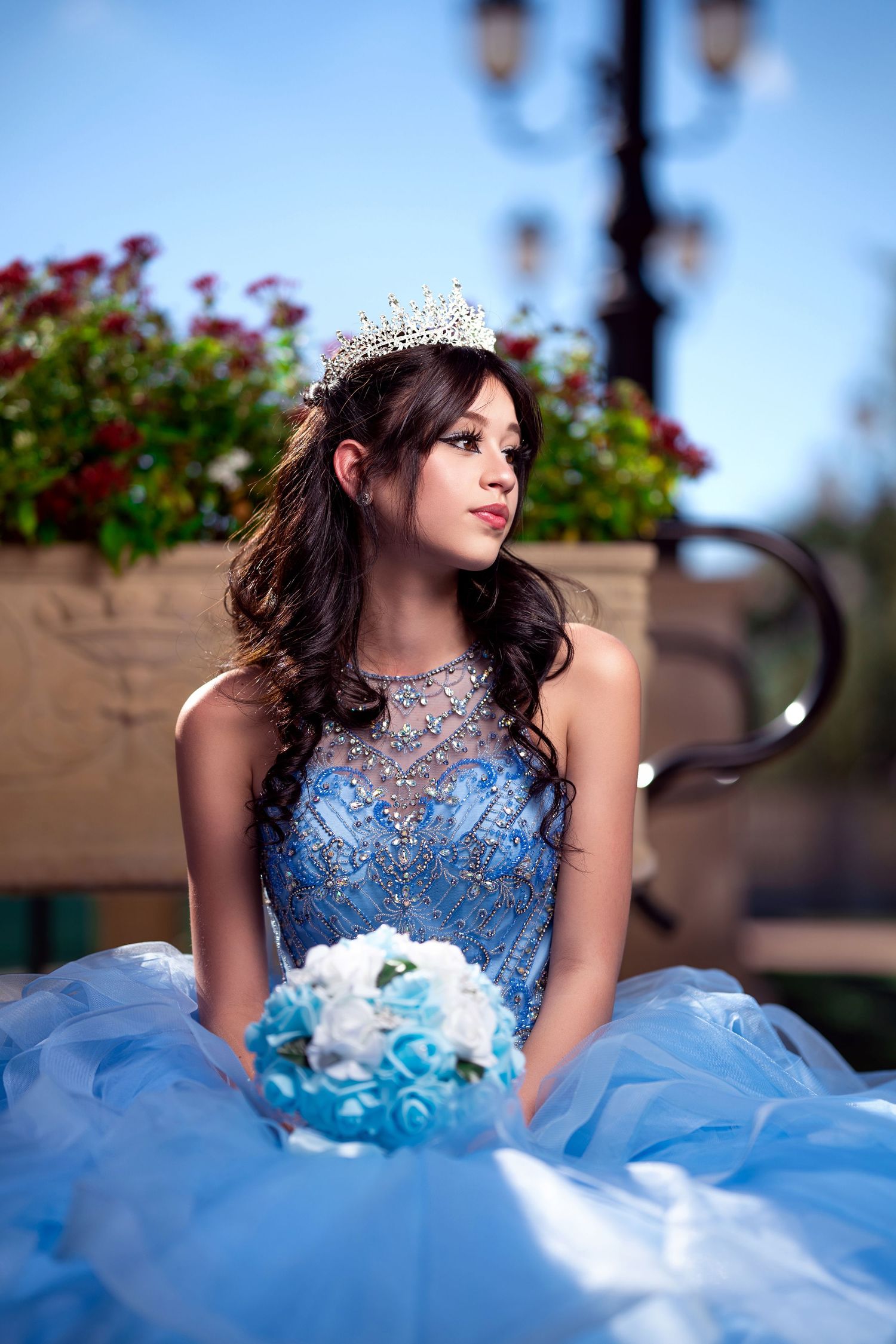 Portrait session of young woman in sparkly blue quinceañera dress on stone terrace.