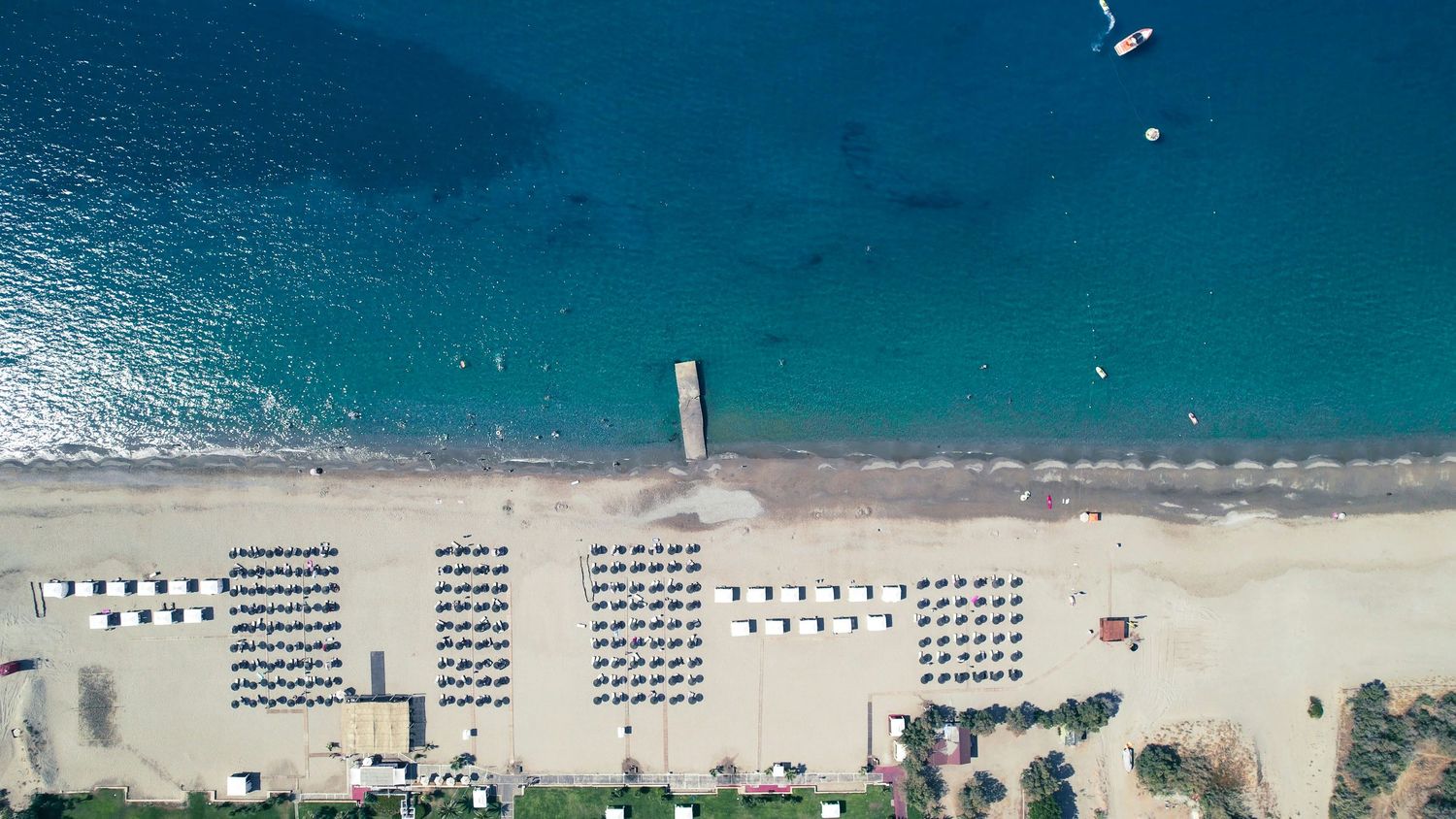 Aerial view of a pristine beach with organized rows of umbrellas and loungers along turquoise Mediterranean waters.