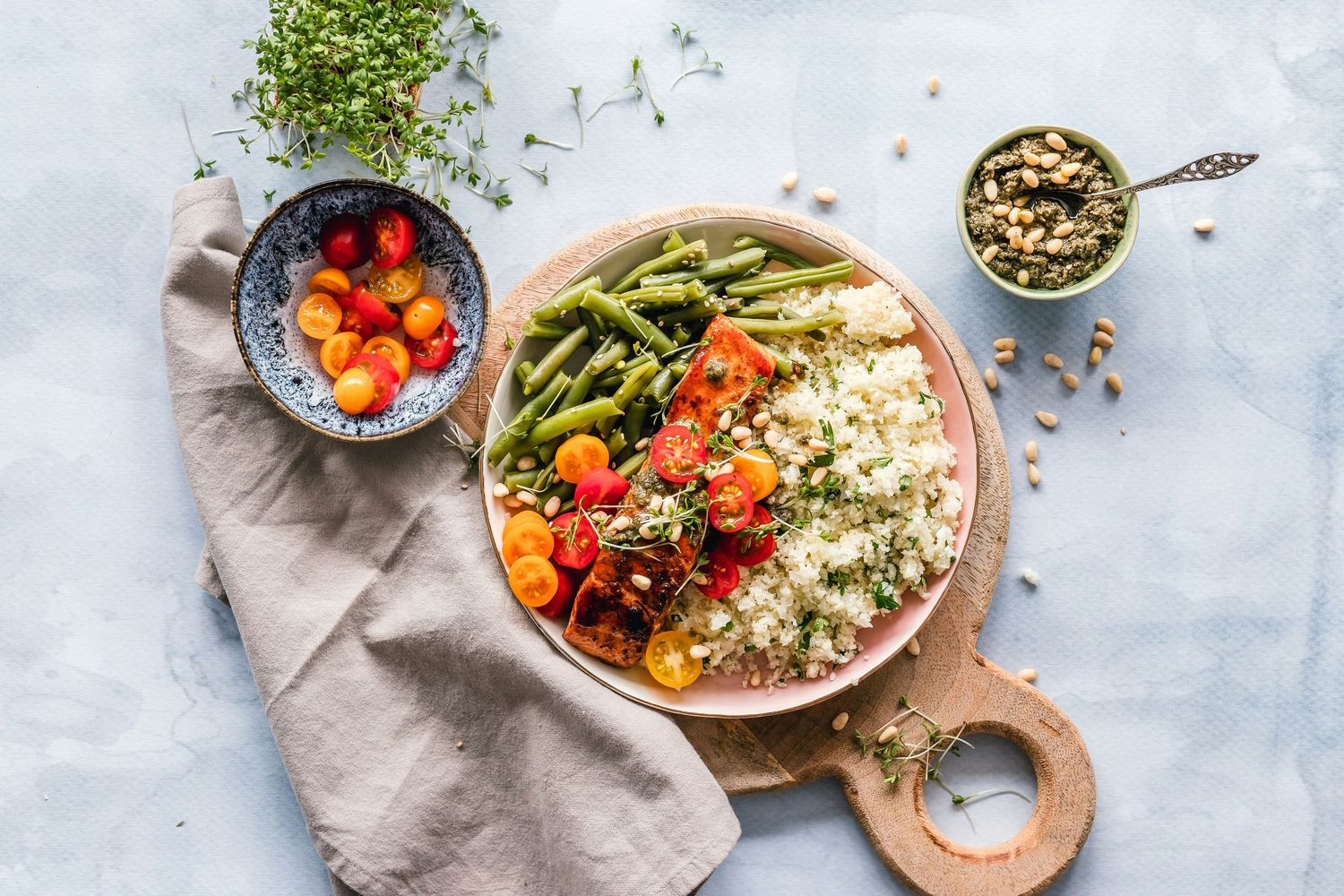 Fresh Mediterranean bowl with quinoa, roasted vegetables, and herbs arranged on light marble surface with serving utensils.