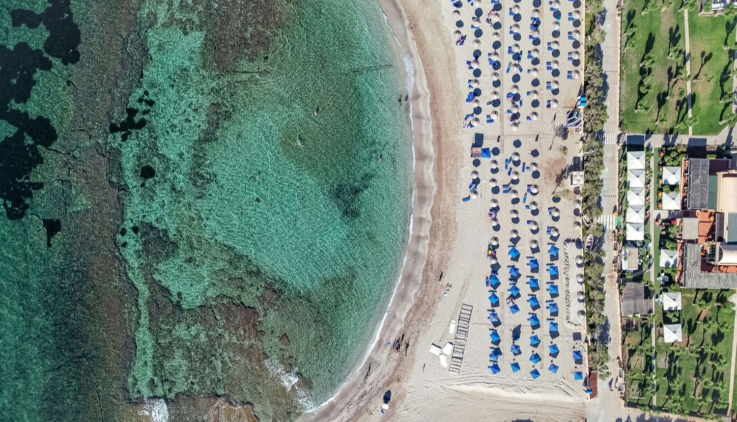 Aerial view of a beach resort with rows of blue and white umbrellas and lounge chairs along the turquoise coastline.