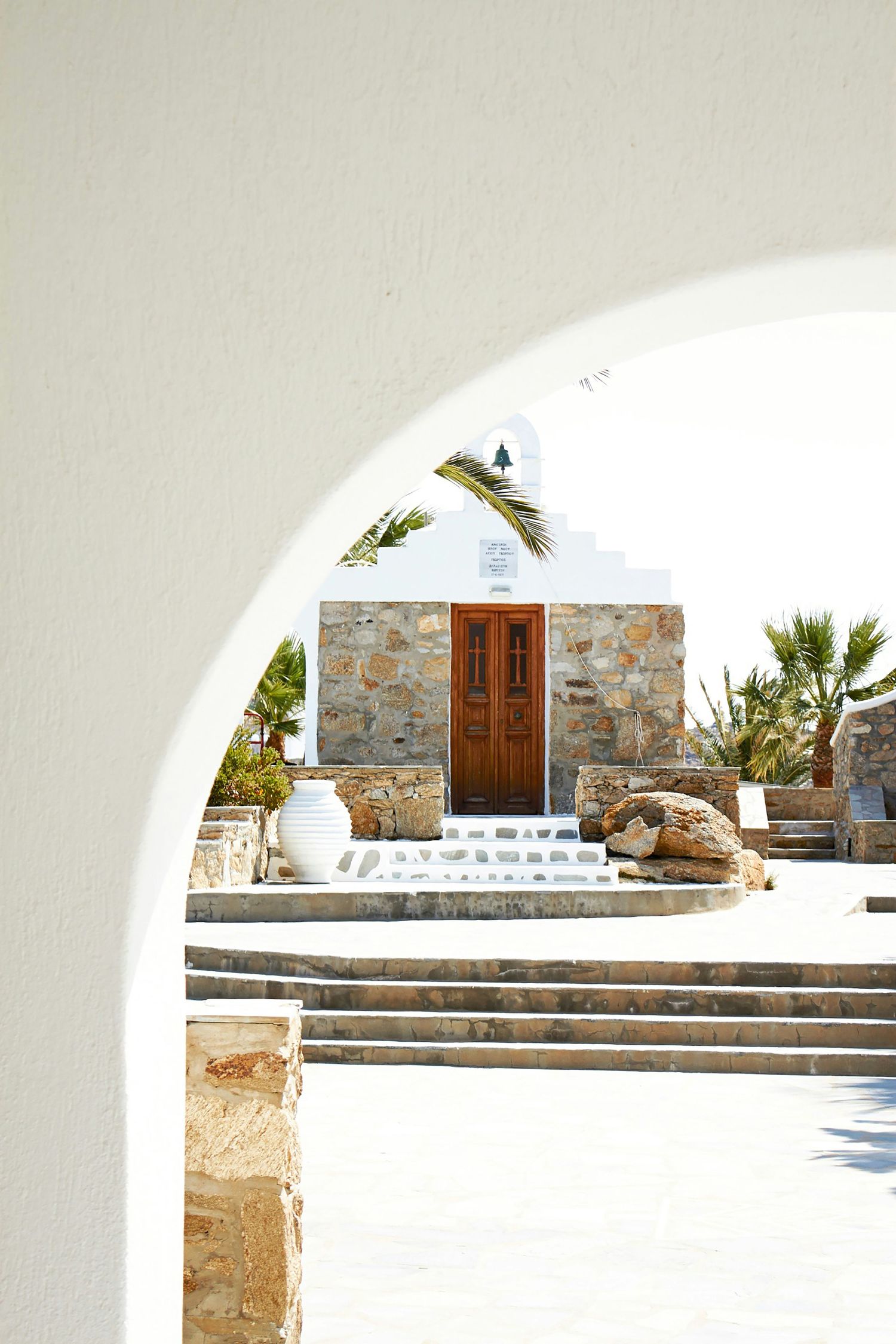 White arched Mediterranean architecture with stone walls and wooden doors leading to elevated terrace steps in Greece.