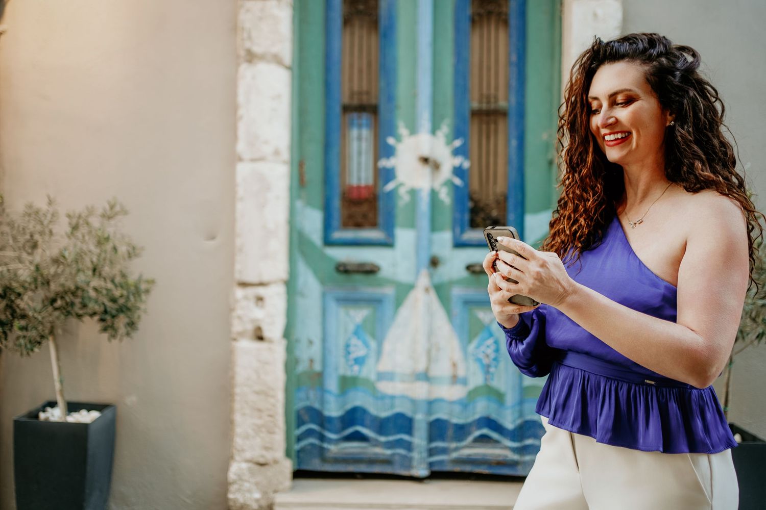 Cristina Nicole Chief Marketing Officer in purple dress dances and twirls gracefully in front of rustic stone wall and blue doors.