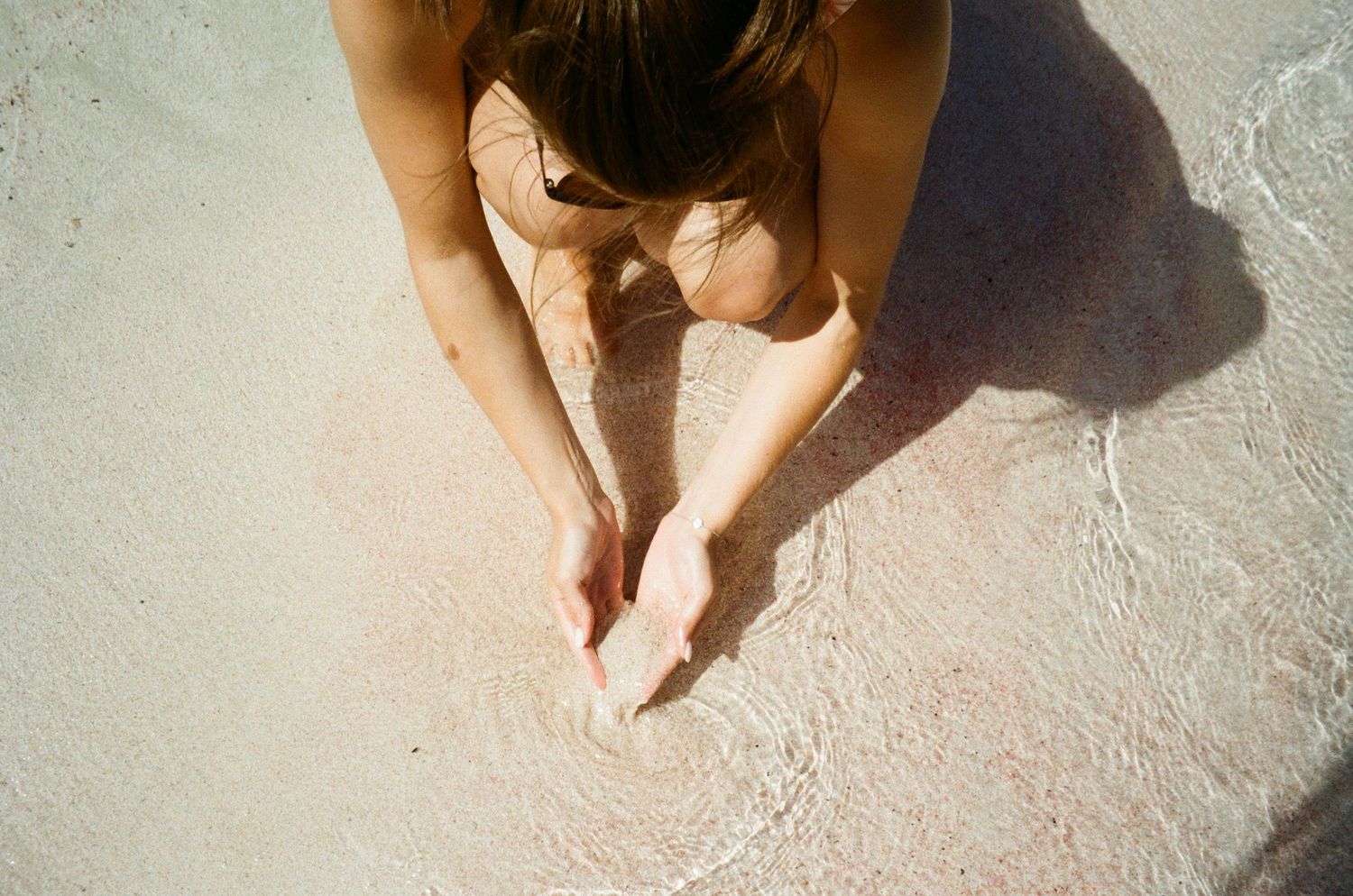 Person drawing in sand on sunny beach creating shadow patterns.