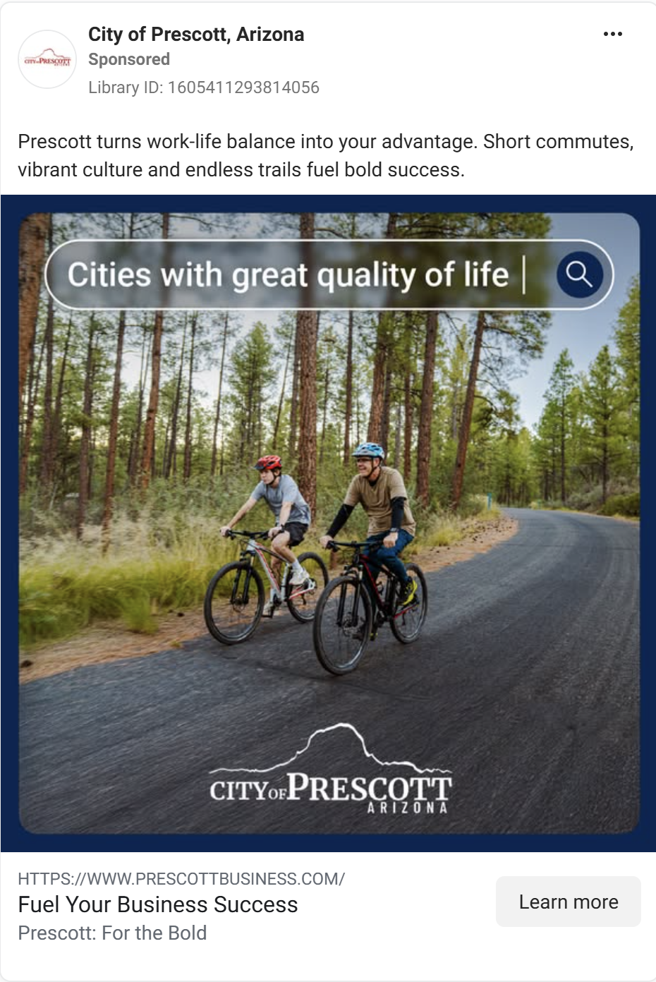 Two cyclists riding mountain bikes on a paved road through tall pine trees in Prescott, Arizona.