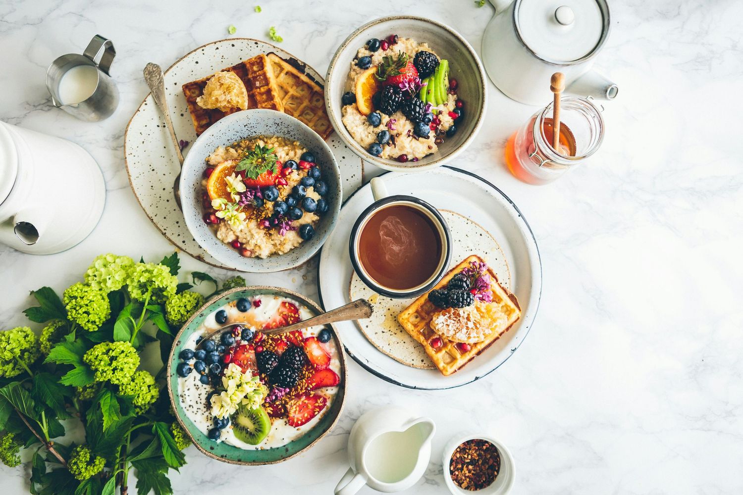 Overhead view of brunch dishes on a white marble table including colorful bowls with eggs, broccoli, and sauces.