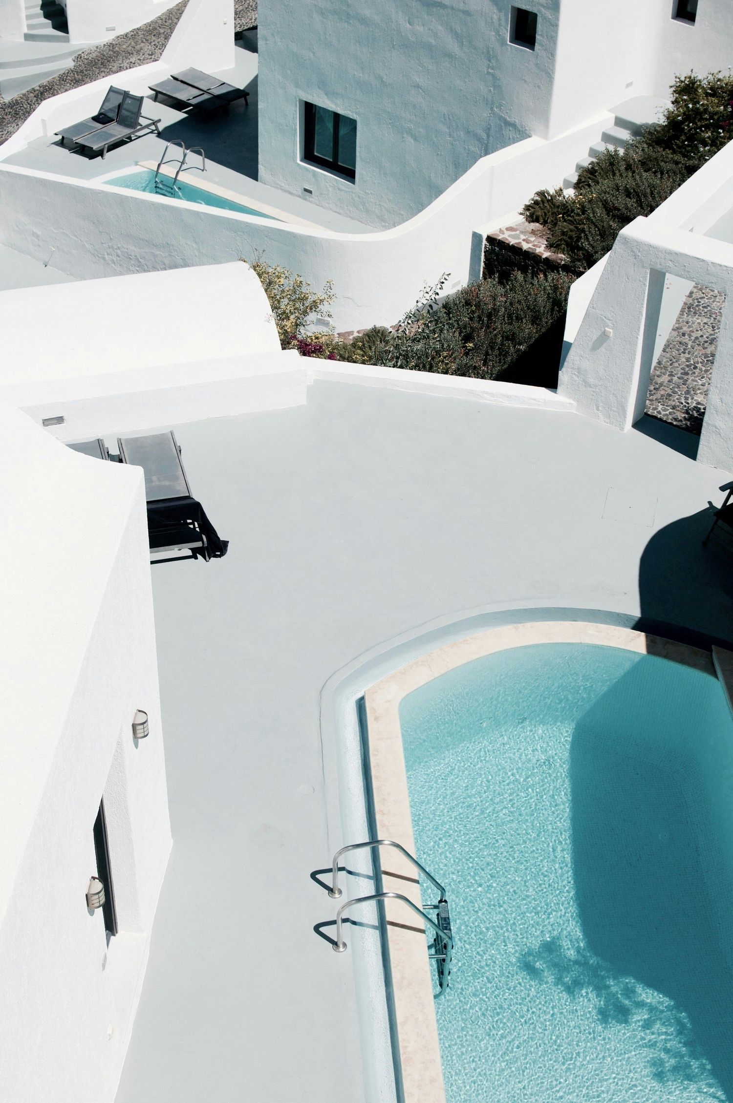 Minimalist white architecture with curved walls and turquoise swimming pools creating a serene Mediterranean aesthetic.
