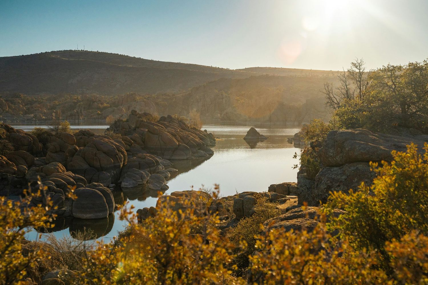 Panoramic landscape view of a scenic lake surrounded by rolling hills and golden autumn foliage at sunset.