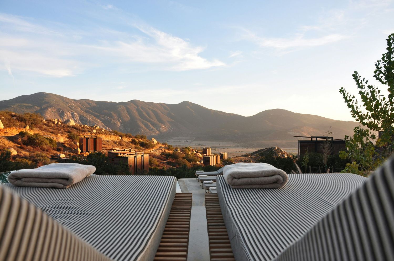 Panoramic view of a modern city skyline with mountains in the background during golden hour sunset.