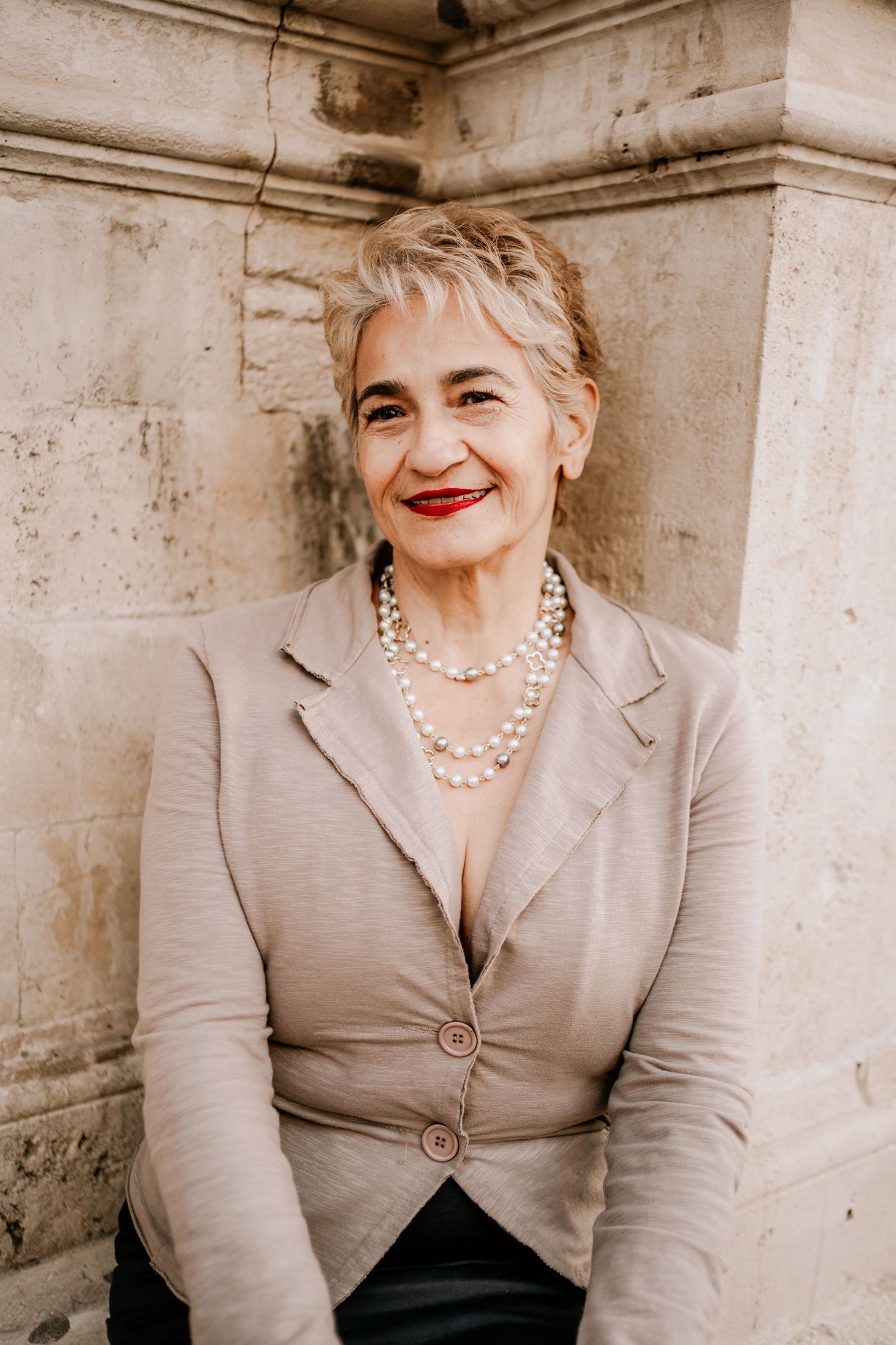 A series of four vintage-style portraits showing someone in a beige blazer and pearl necklace against a stone wall.