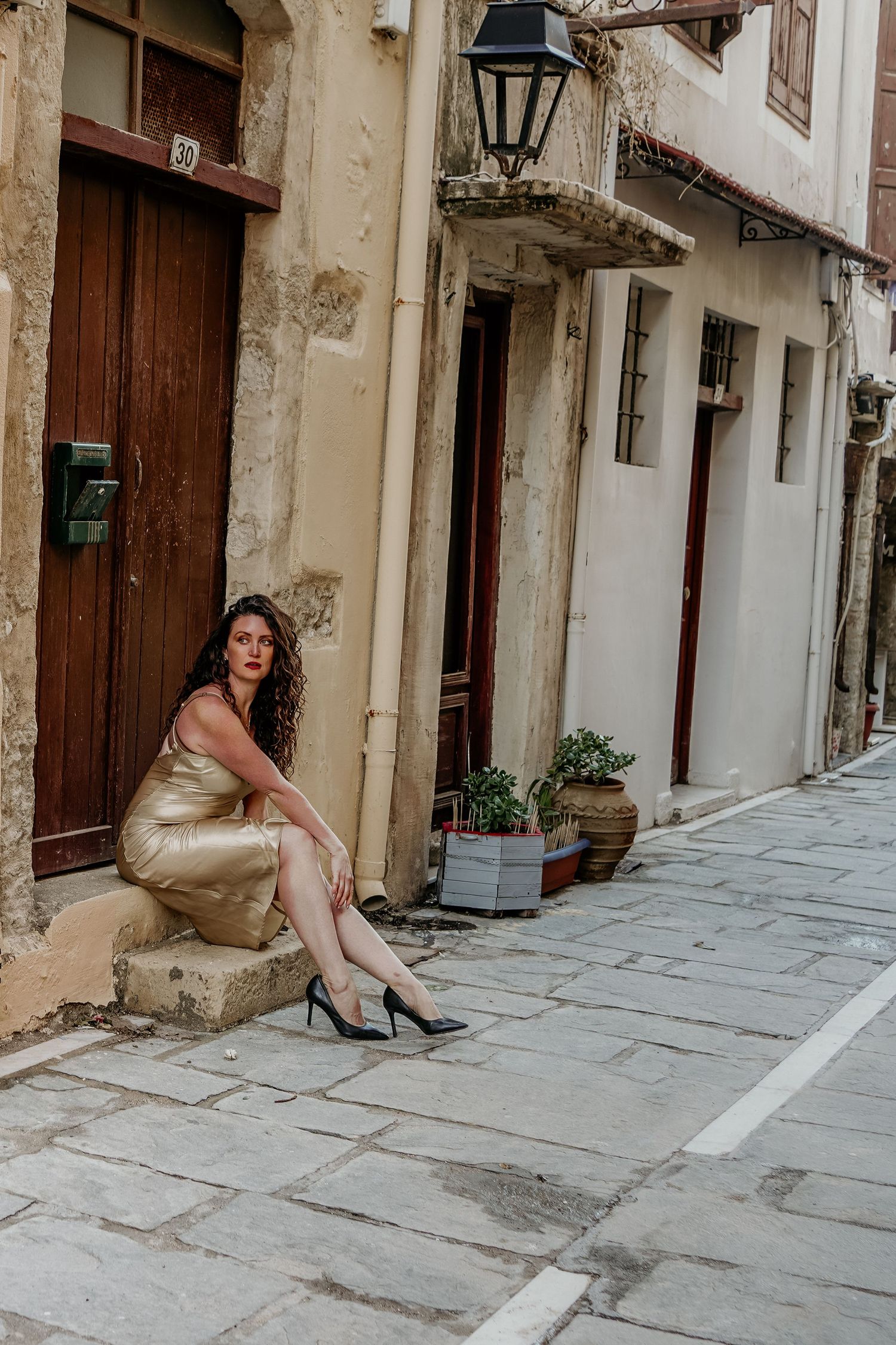 Cristina Nicole Chief Marketing Officer in a gold dress and heels poses dramatically on a historic stone street with rustic wooden doors.