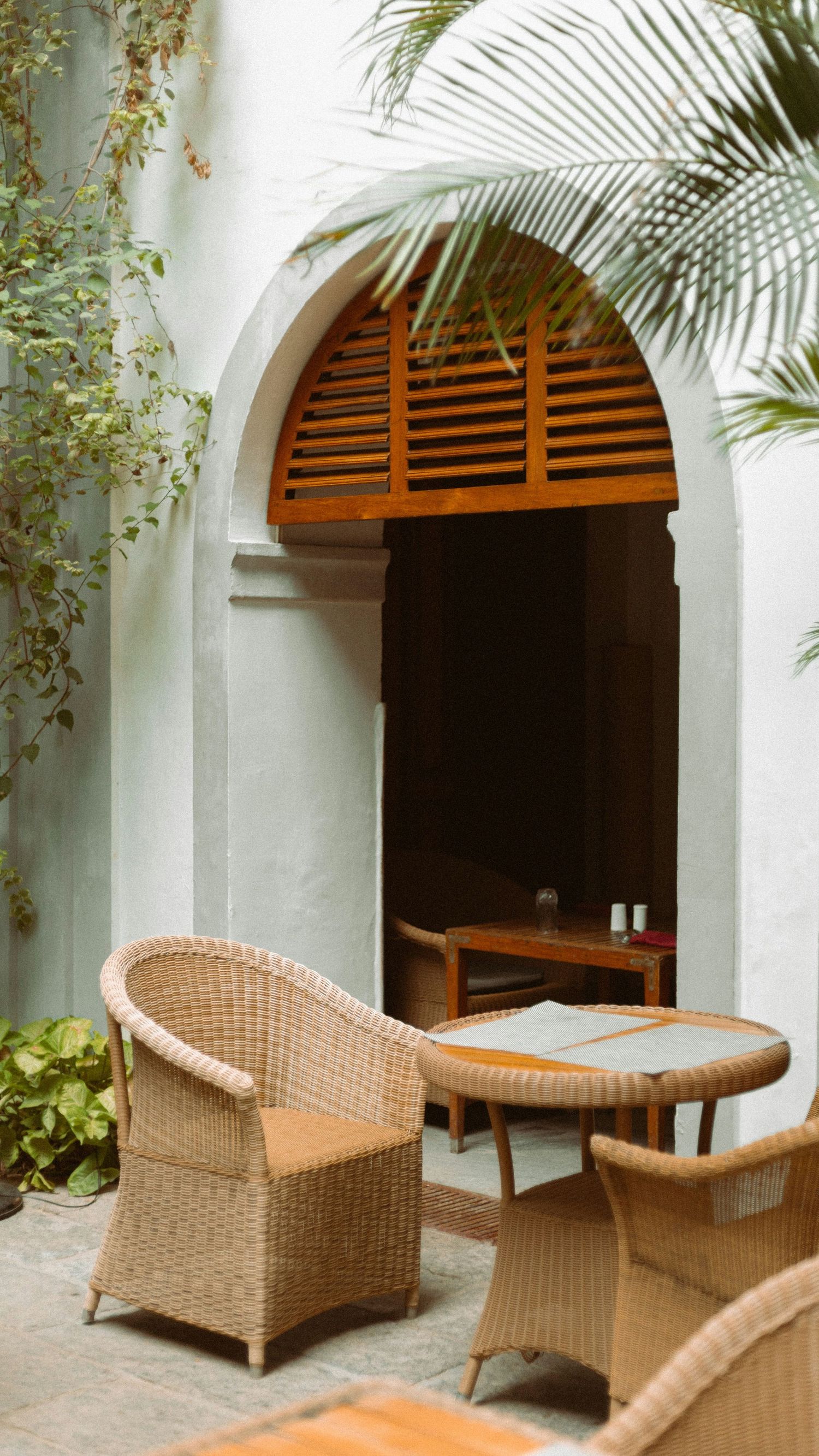 Wicker patio furniture arranged on a terrace with white arched doorways and tropical plants creating a serene outdoor space.