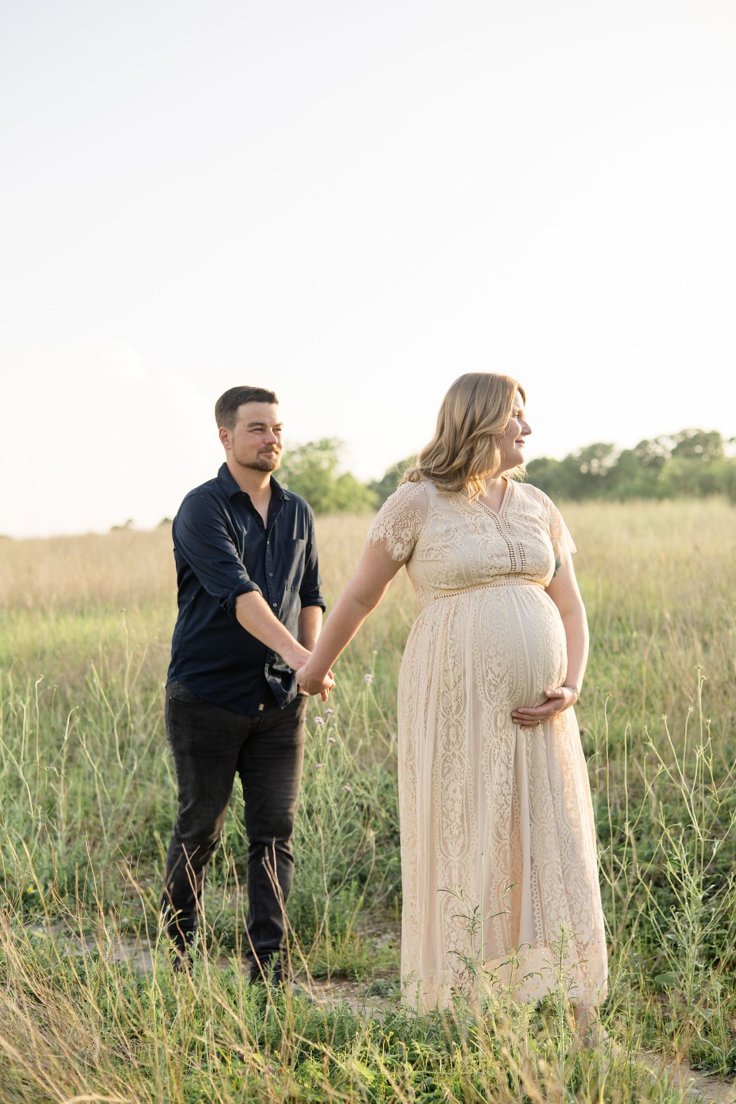 mom and dad walk hand in hand during maternity portrait session in the spring at erwin park in mckinney texas