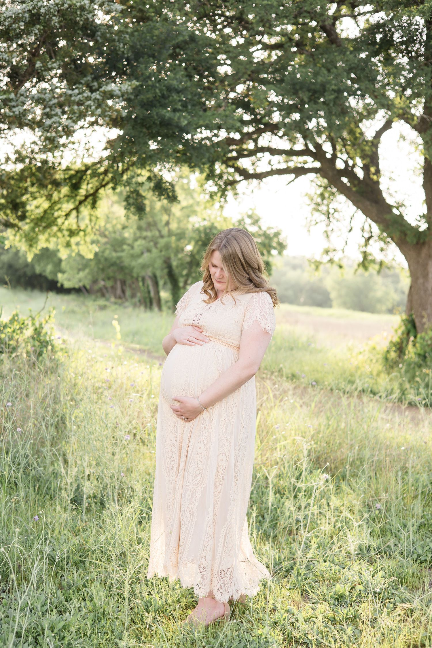 expecting mother in cream lace dress poses during maternity portrait session at golden hour at erwin park in mckinney texas