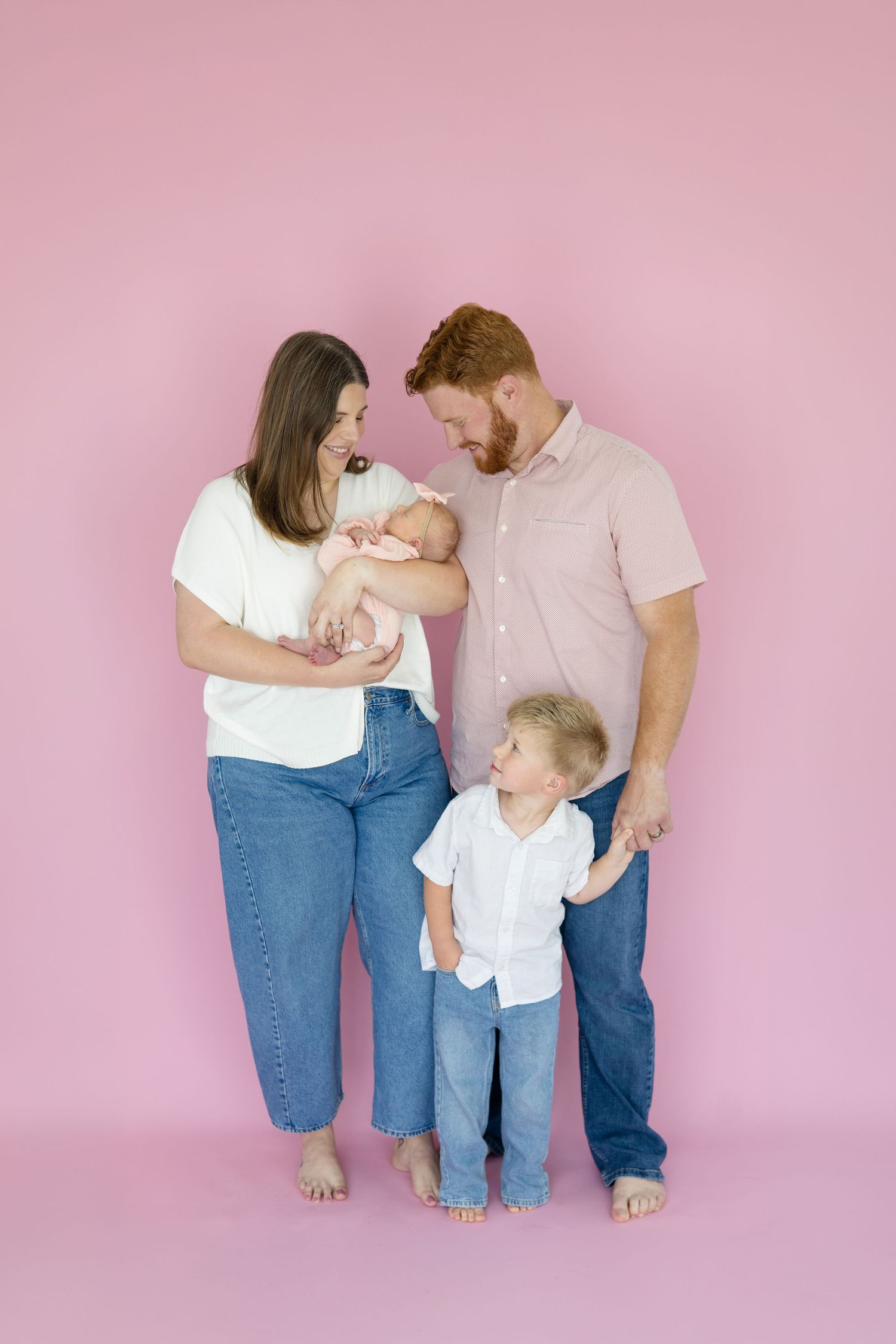 Family of 4 poses together in front of pink wall during lifestyle newborn session in the studio with family photographer based in McKinney