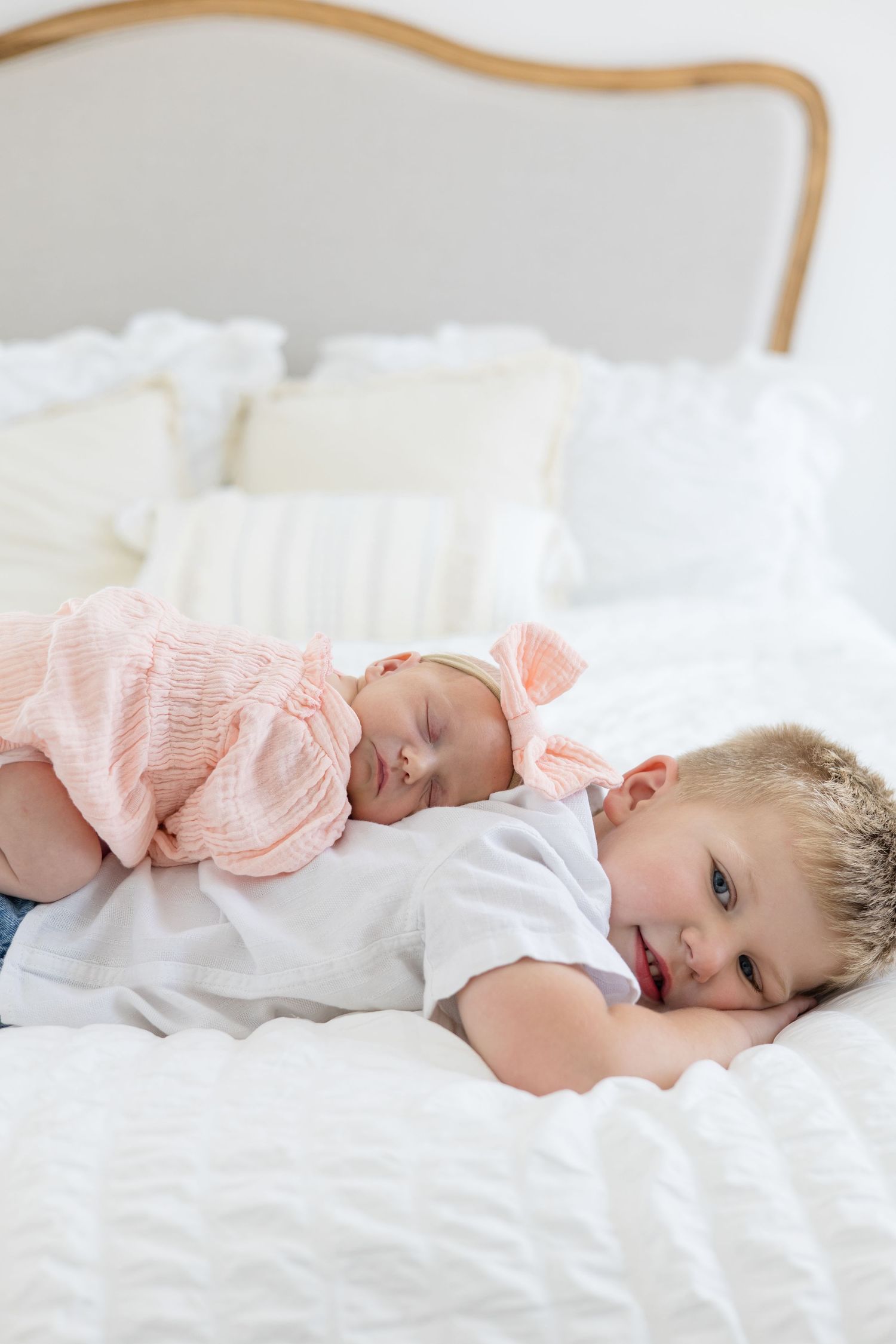 Newborn baby girl in pink outfit and bow lays on back of older brother in white button up during lifestyle newborn session in McKinney Texas