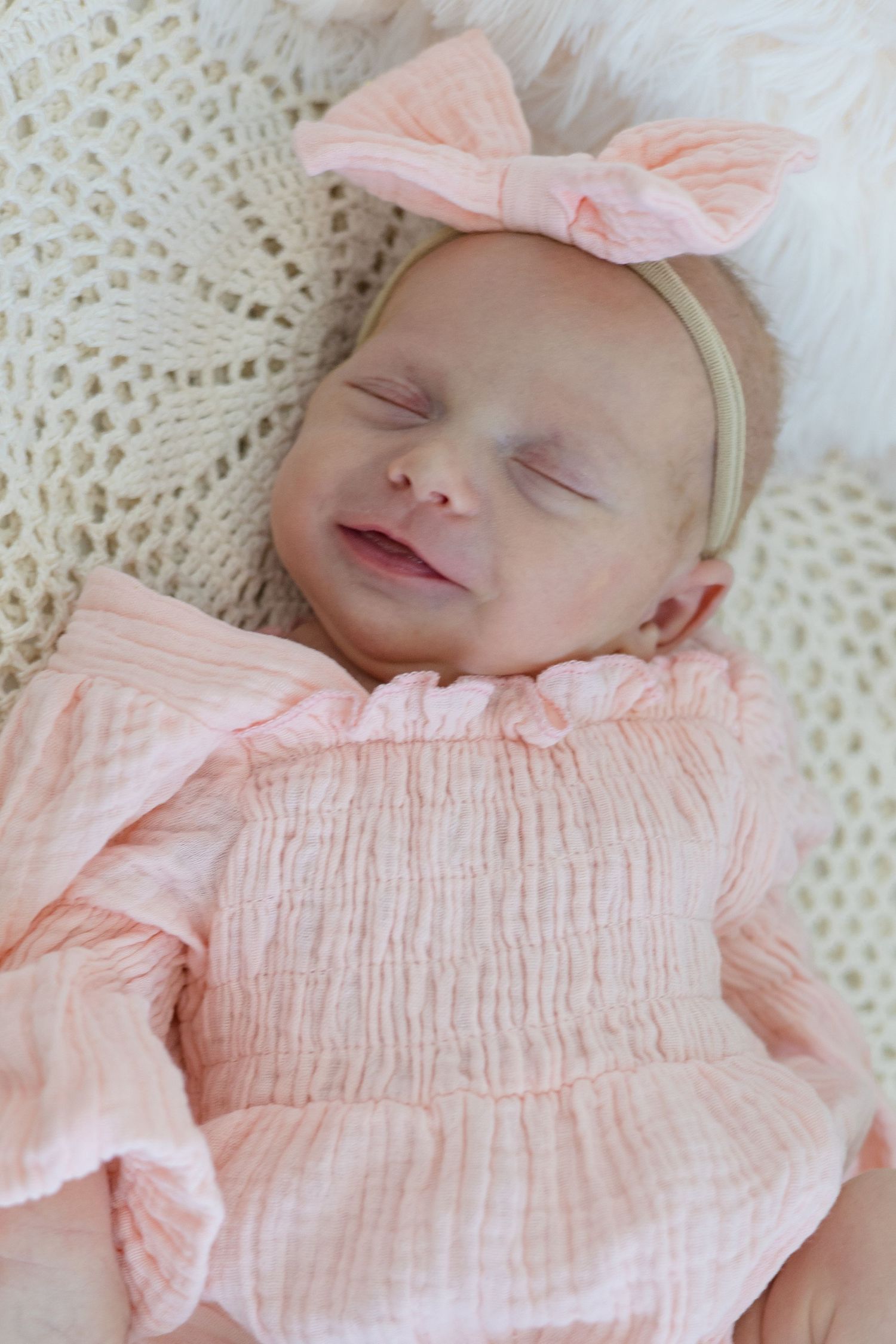 Newborn baby girl in pink outfit smiles while sleeping during lifestyle newborn session in the summer with McKinney photographer