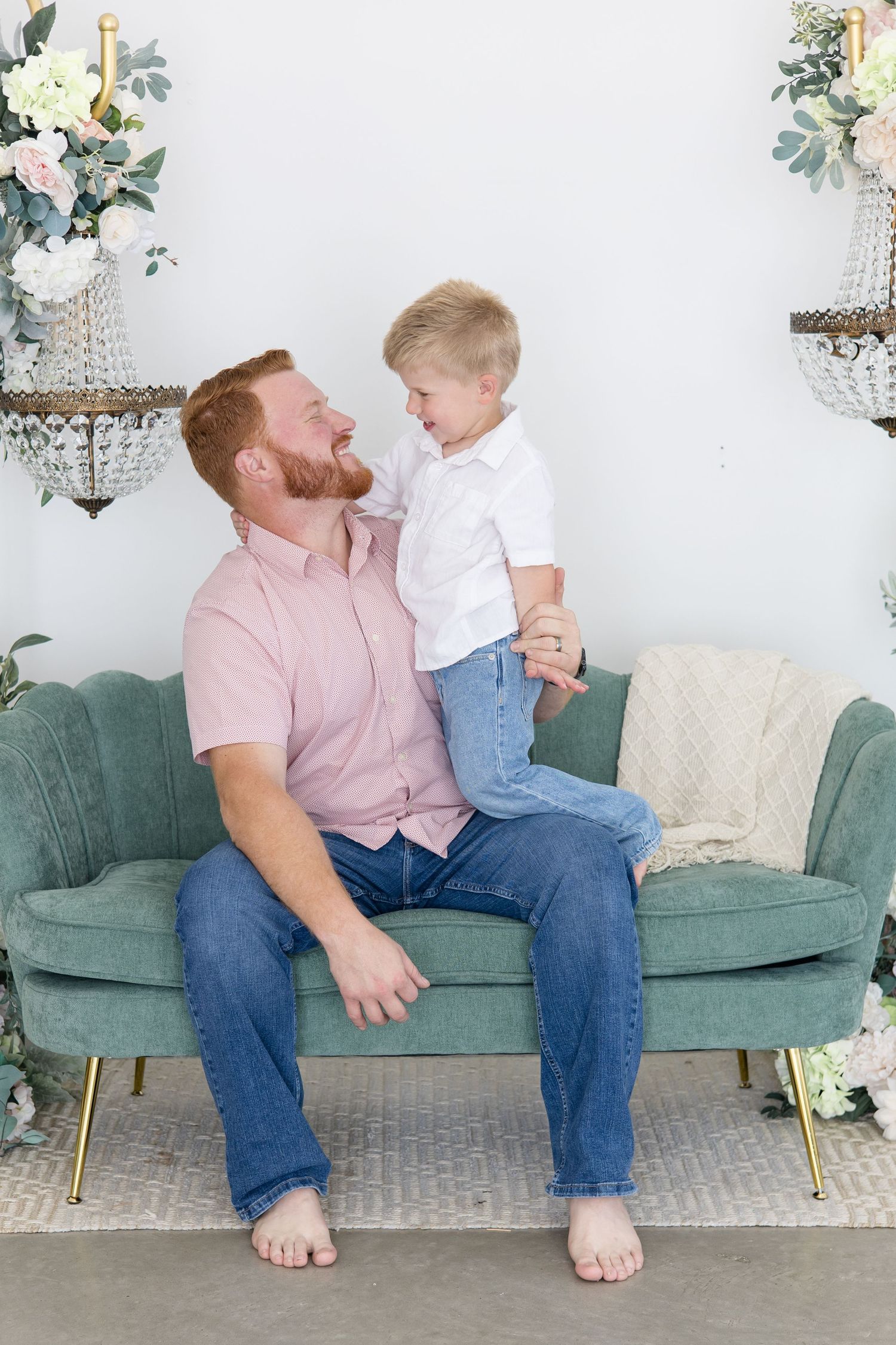 Dad and son pose together on green couch in studio with Newborn photographer Reagan Marie Photography