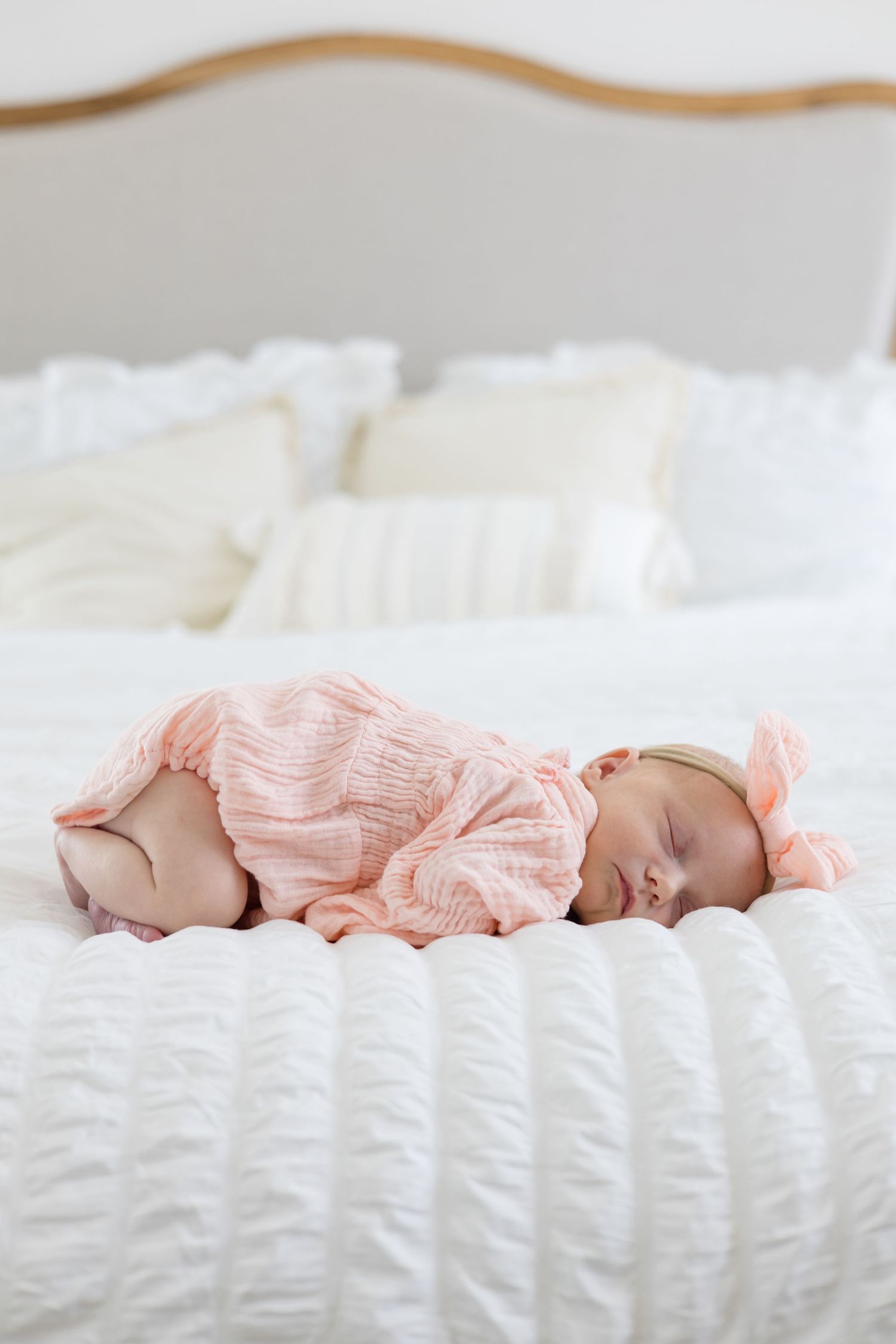 Newborn baby girl lays on belly in pink outfit and bow on white bed during lifestyle newborn session in the summer with McKinney photographe
