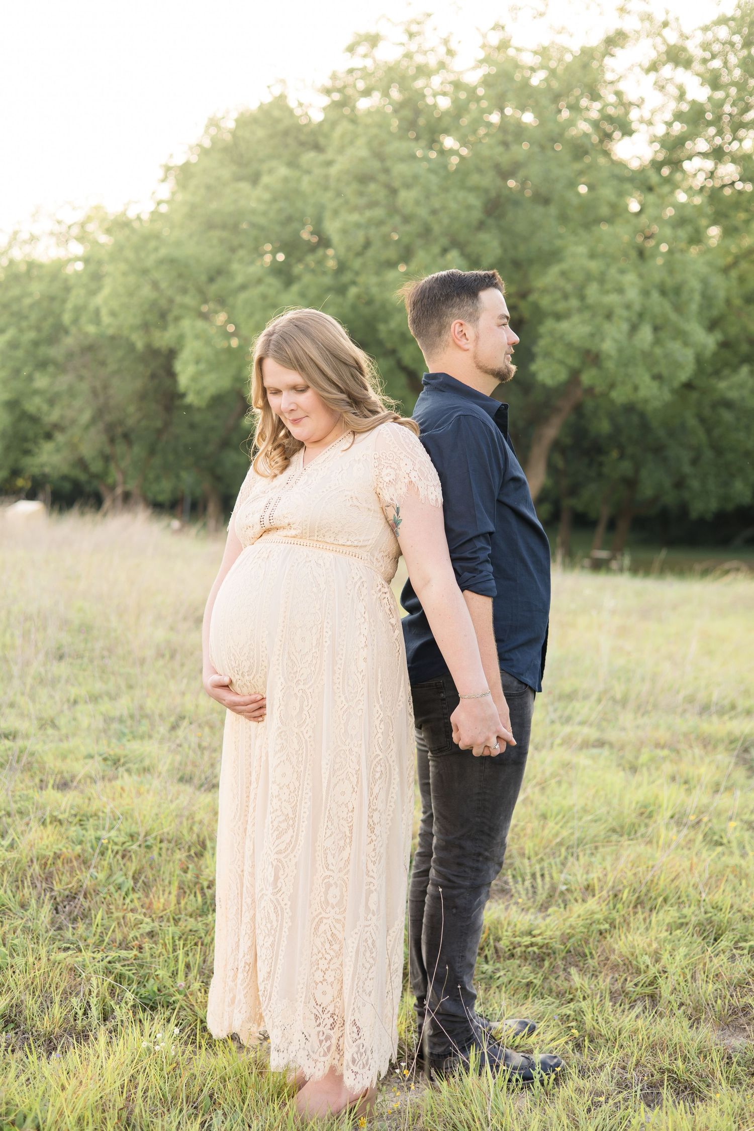 expecting parents stand back to back during maternity session at erwin park with mckinney maternity photographer