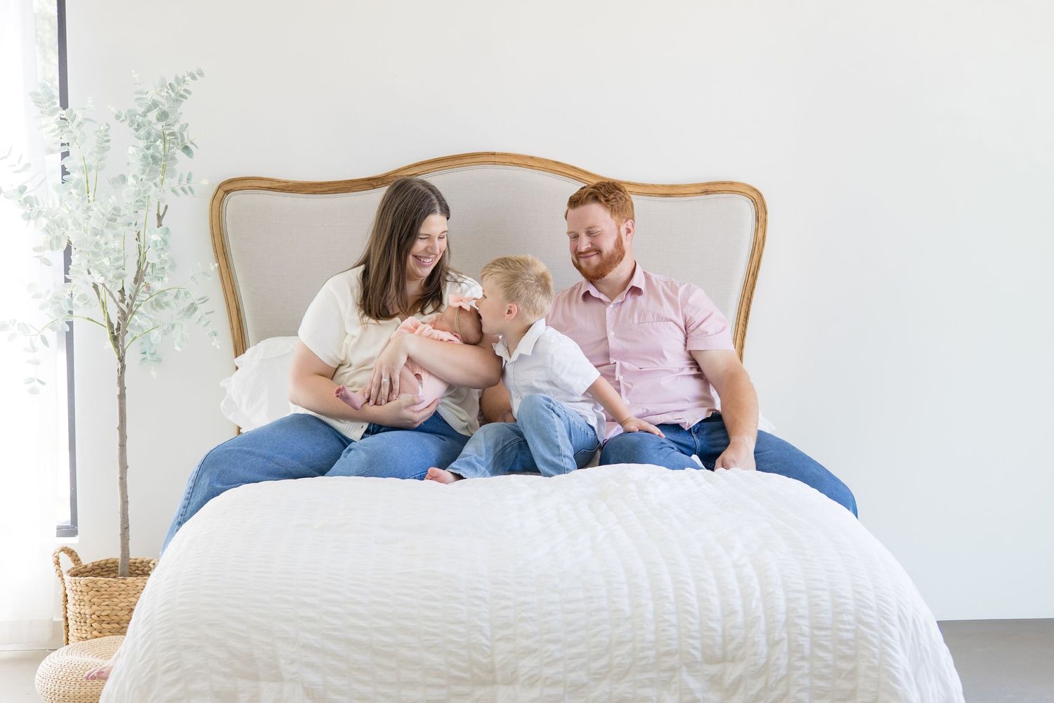 Family of 4 poses together on bed in studio in McKinney Texas with photographer Reagan Marie Photography for lifestyle newborn session