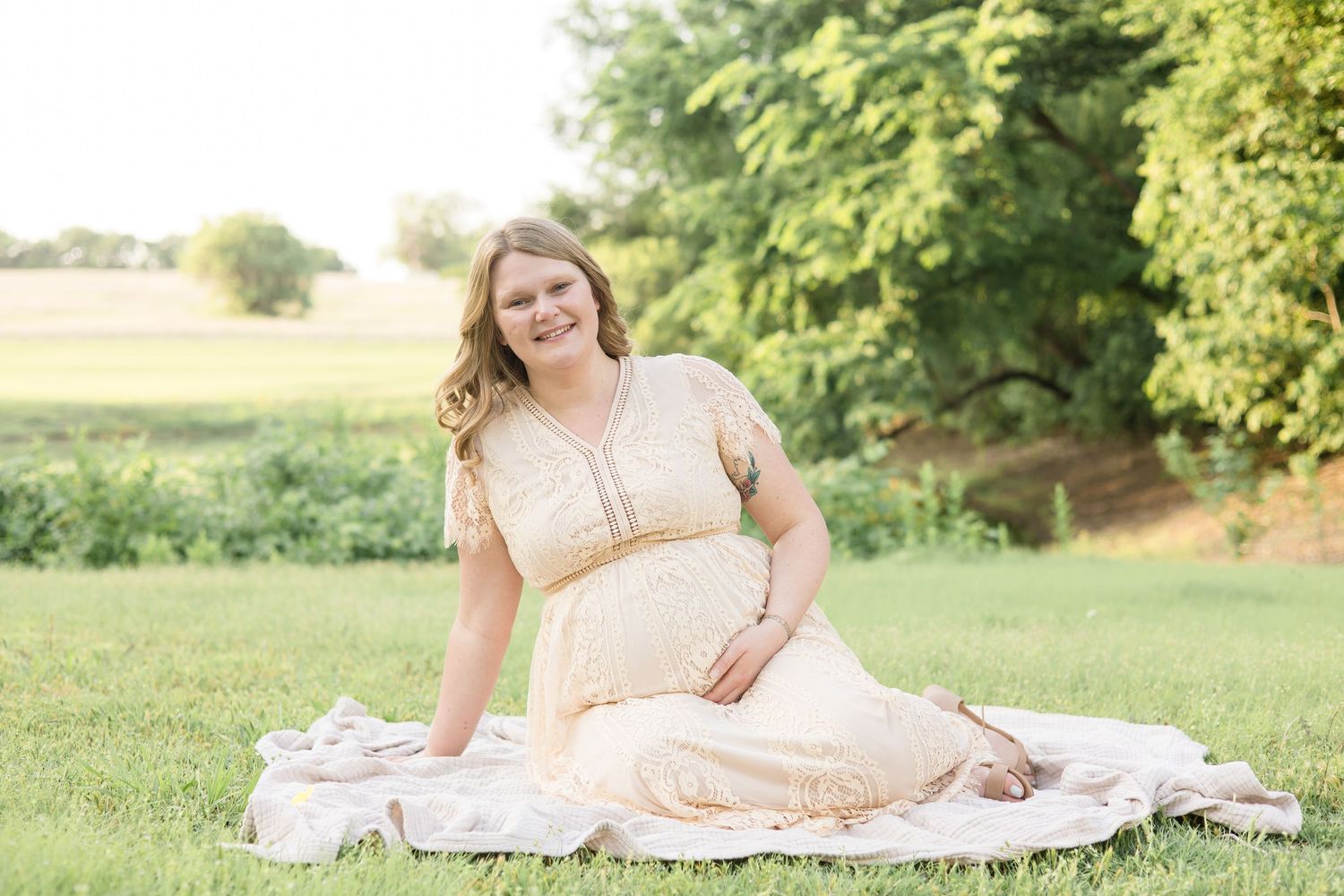 expecting mother sits on blanket in front of pond at erwin park during maternity session with mckinney based photographer