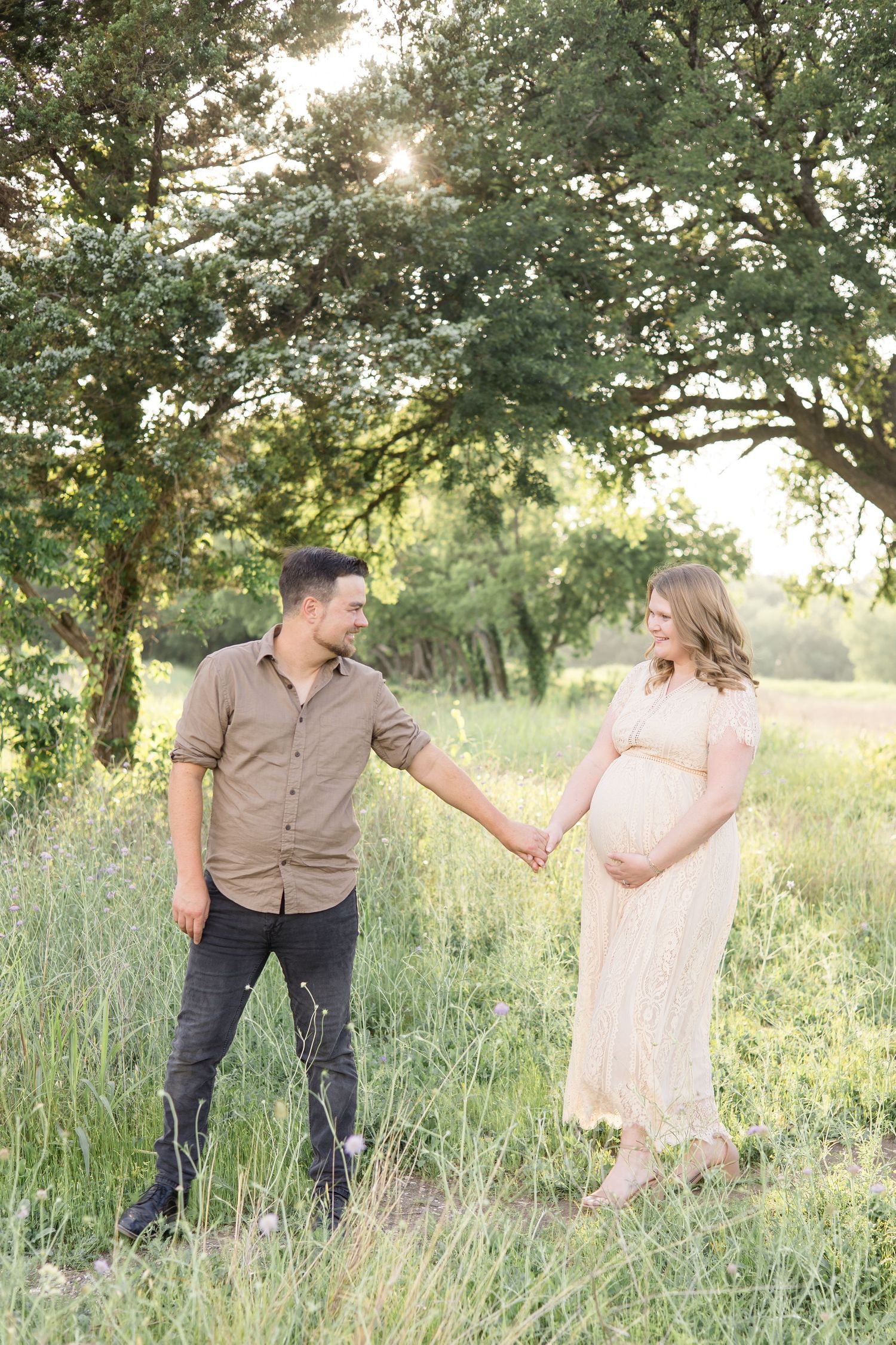 mom and dad walk hand in hand, looking at each other, during maternity portrait session in the spring at erwin park in mckinney texas