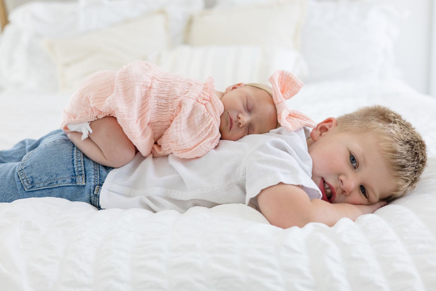 Newborn baby girl in pink outfit and bow lays on back of older brother in white button up during lifestyle newborn session in McKinney Texas