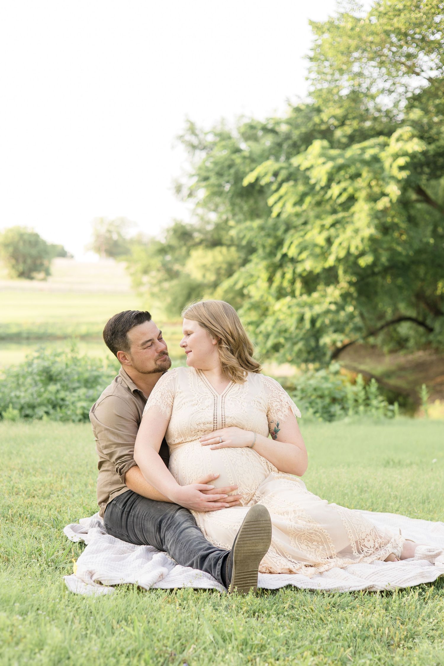 mom in tan dress looks at dad in beige shirt and black pants during maternity session in mckinney texas at erwin park